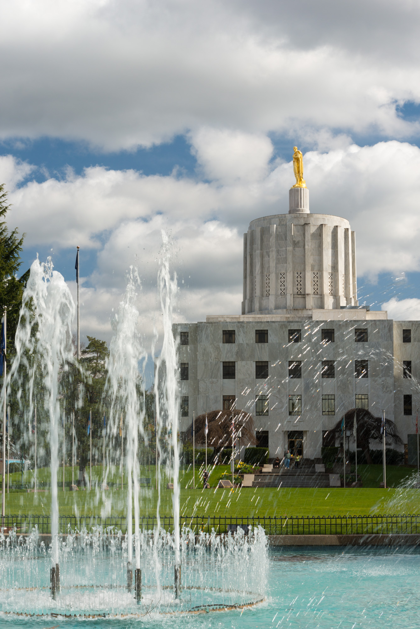 Oregon State Capitol building with gold pioneer statue on dome and a fountain in the foreground.