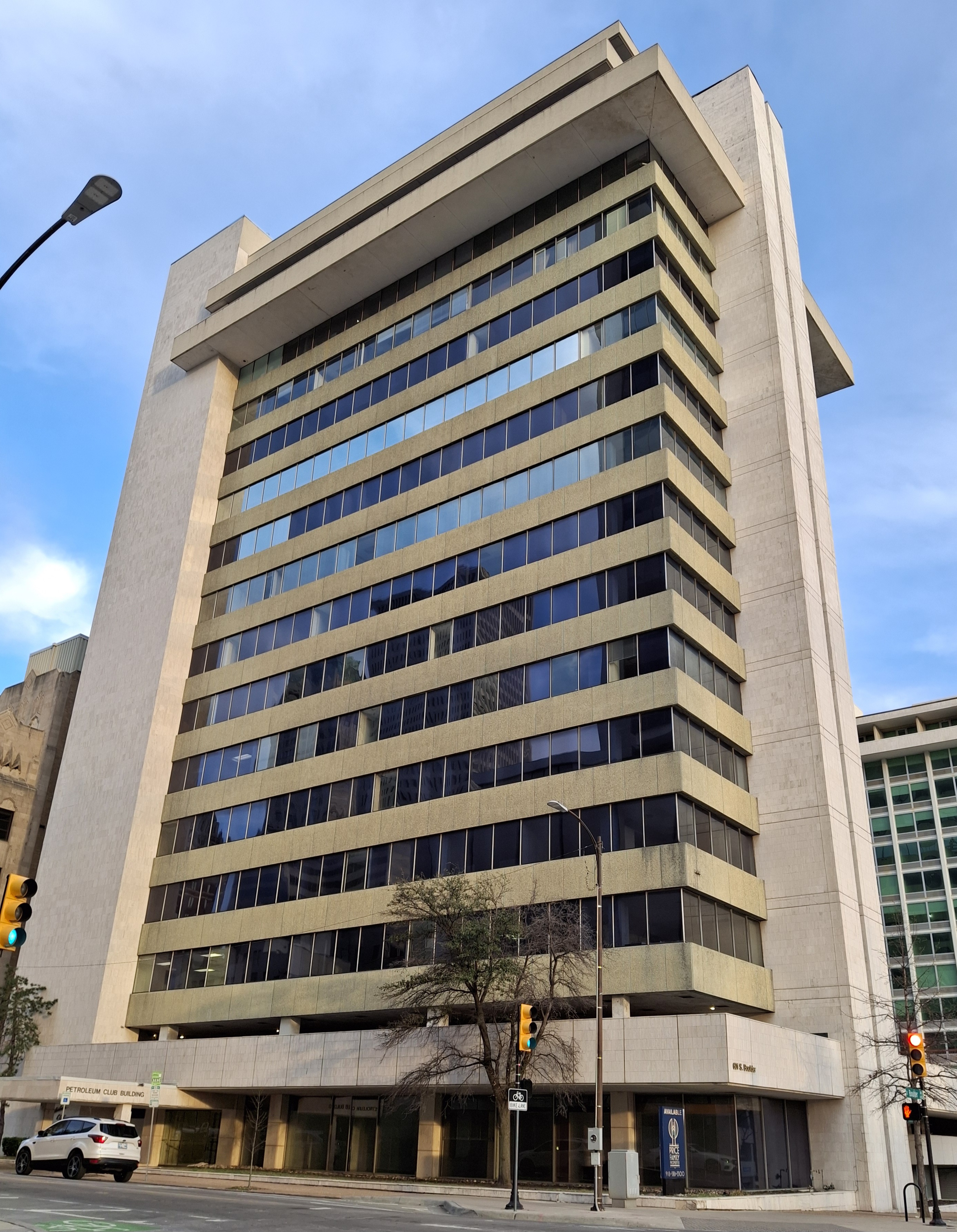 Sixteen-story concrete and glass office tower photographed from a street corner below.