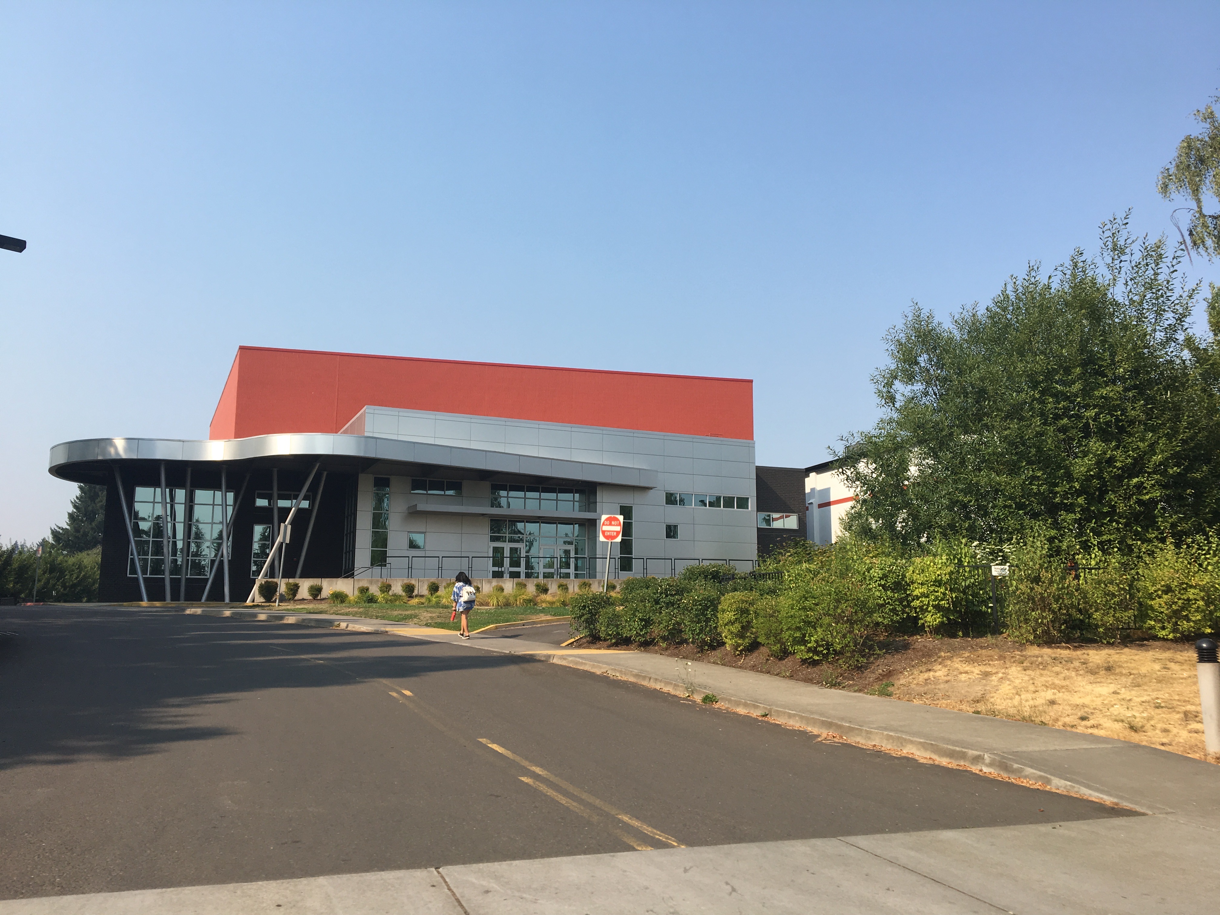 Modern school building with a curved glass entrance canopy and red upper facade.