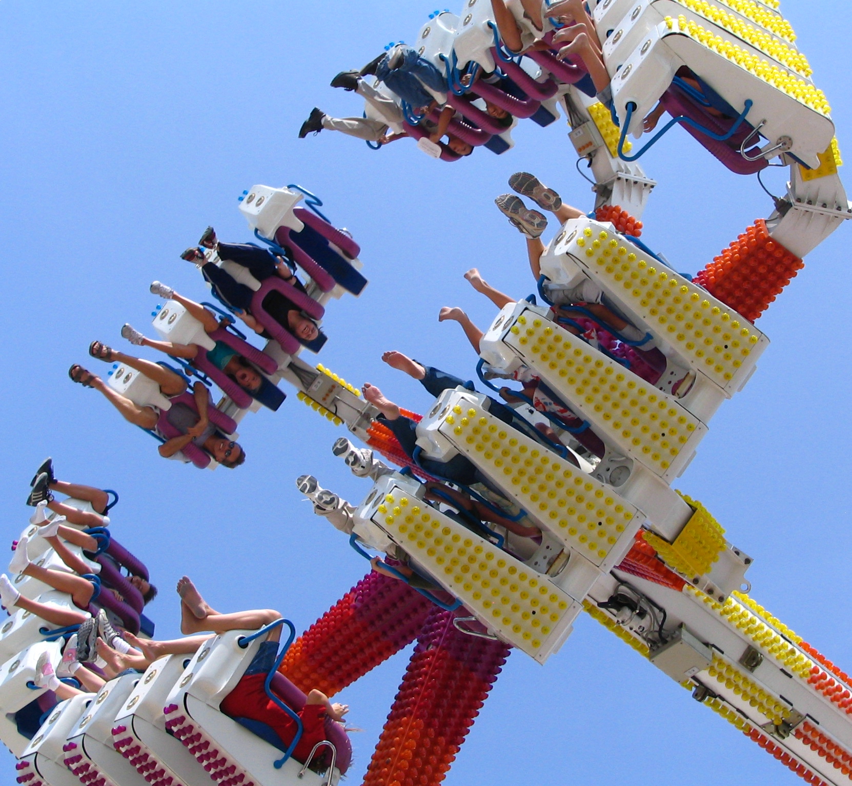 Riders suspended upside down on a colorful spinning thrill ride against a clear blue sky.