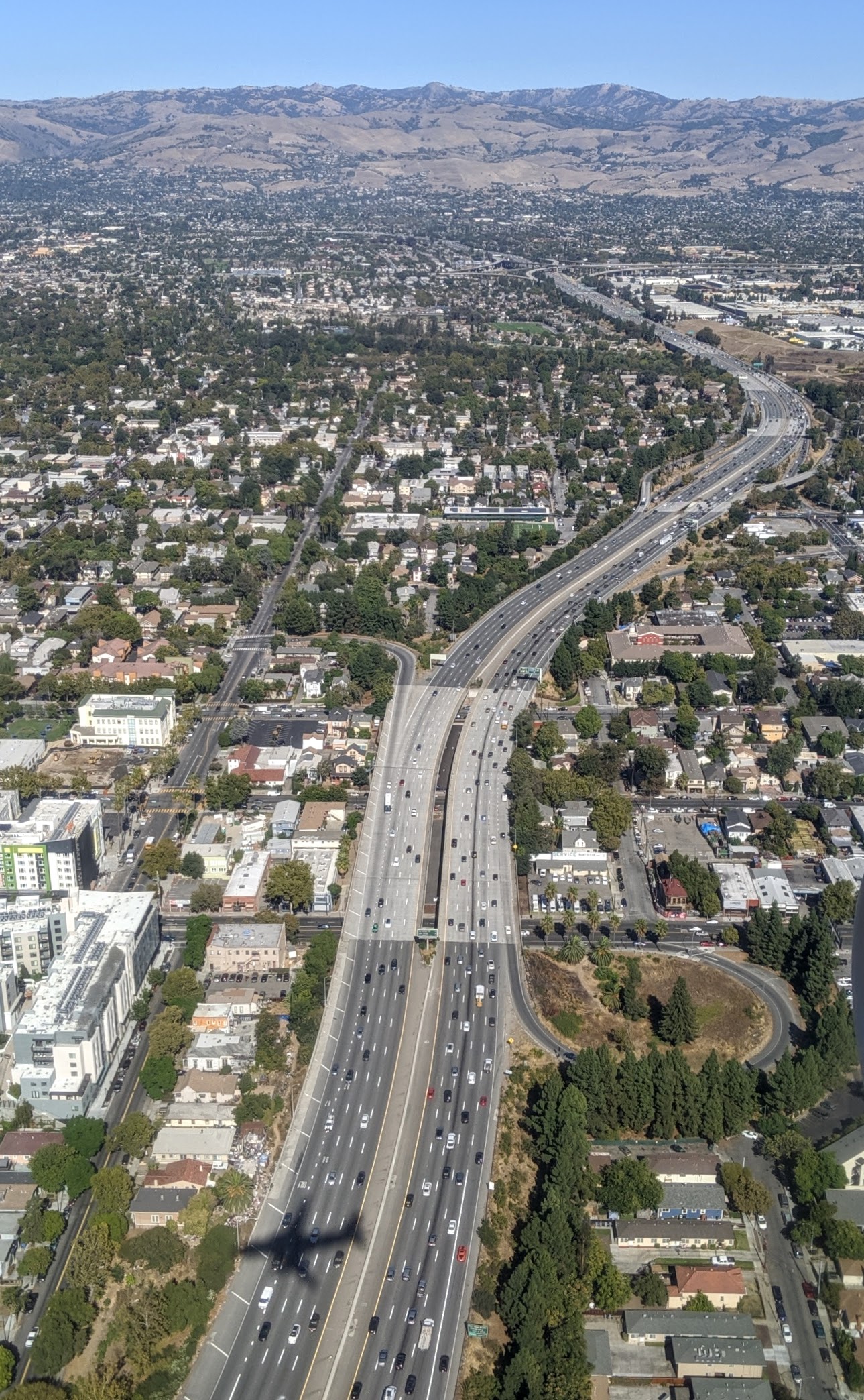 Aerial view of a multi-lane freeway with a wide center median and tree-lined neighborhoods on both sides.