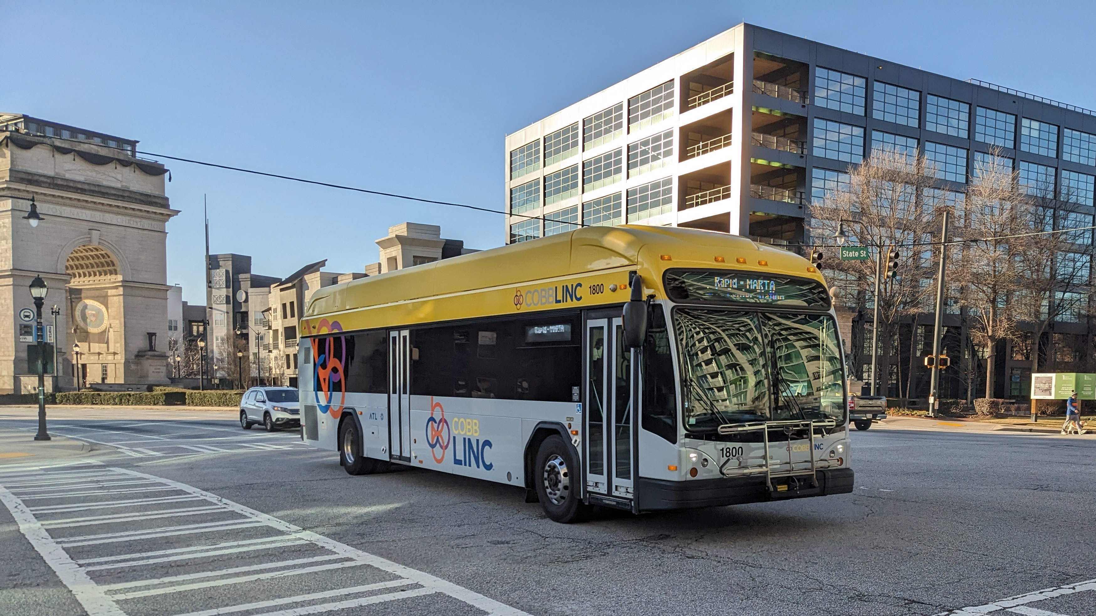 A yellow and white CobbLinc transit bus at an urban intersection.