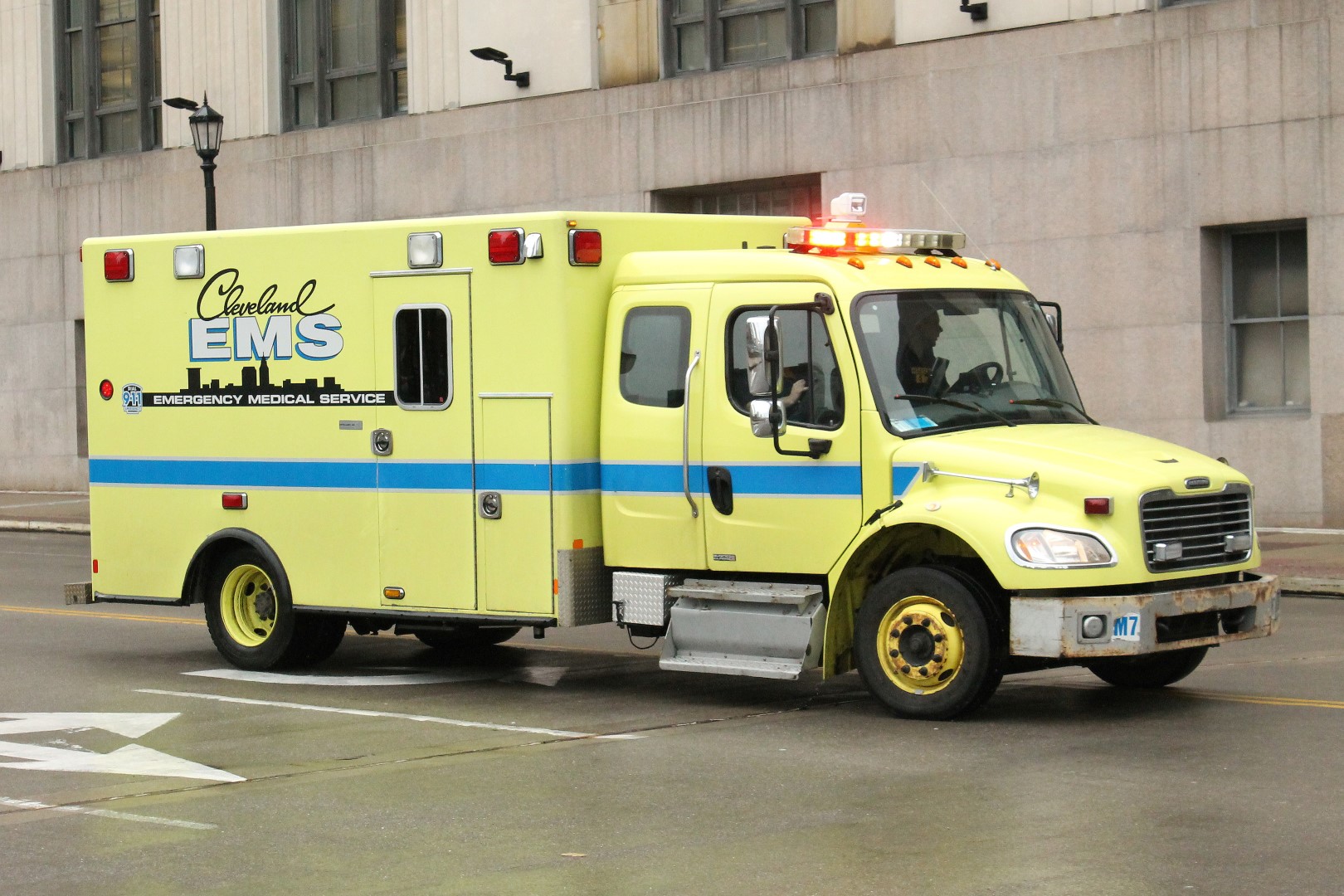 A yellow-green EMS ambulance with emergency lights on drives down a city street.