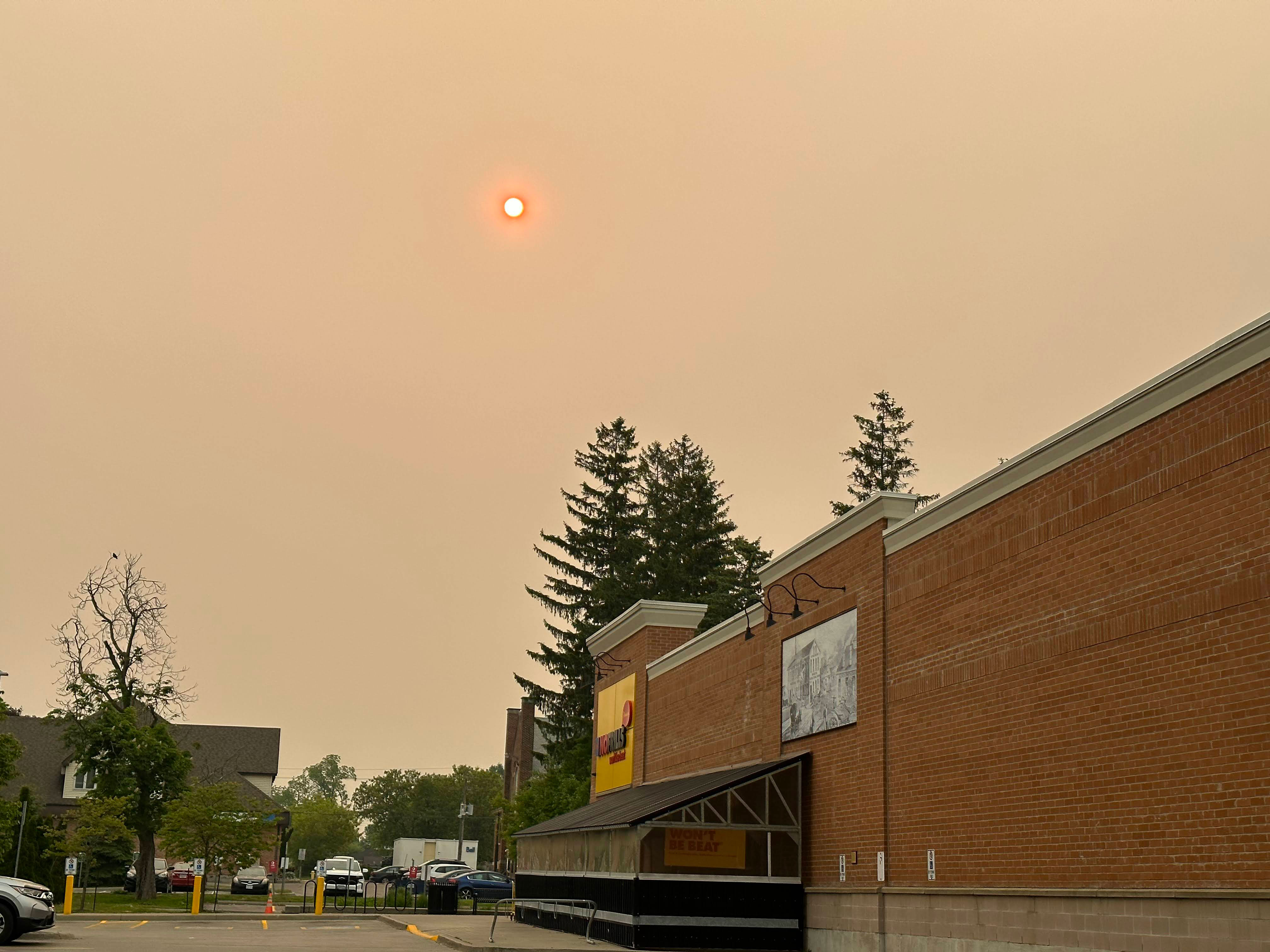 Red sun visible through a thick orange haze above trees and a building.