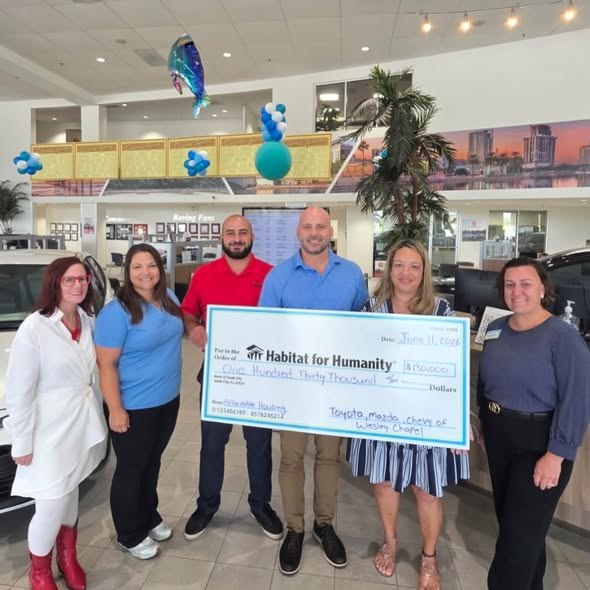 Six people holding a large ceremonial check for $130,000 inside a car dealership showroom.