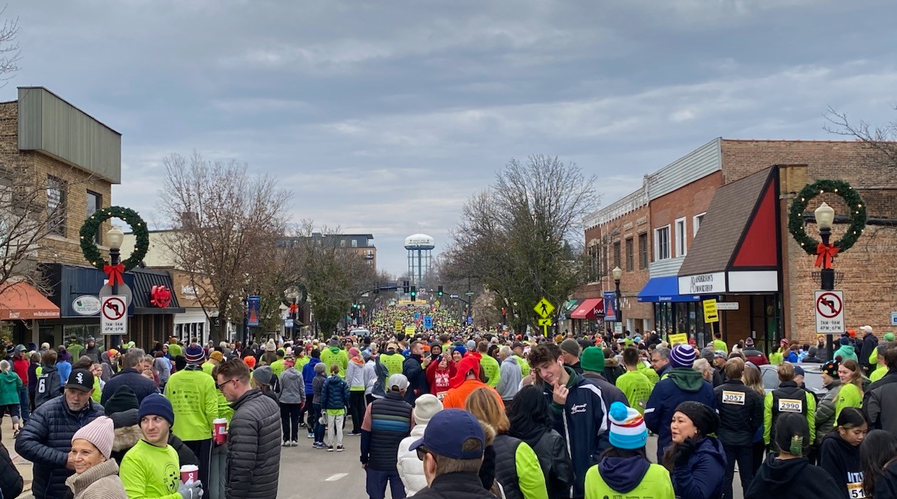 Crowd filling a downtown street lined with brick storefronts and holiday decorations.