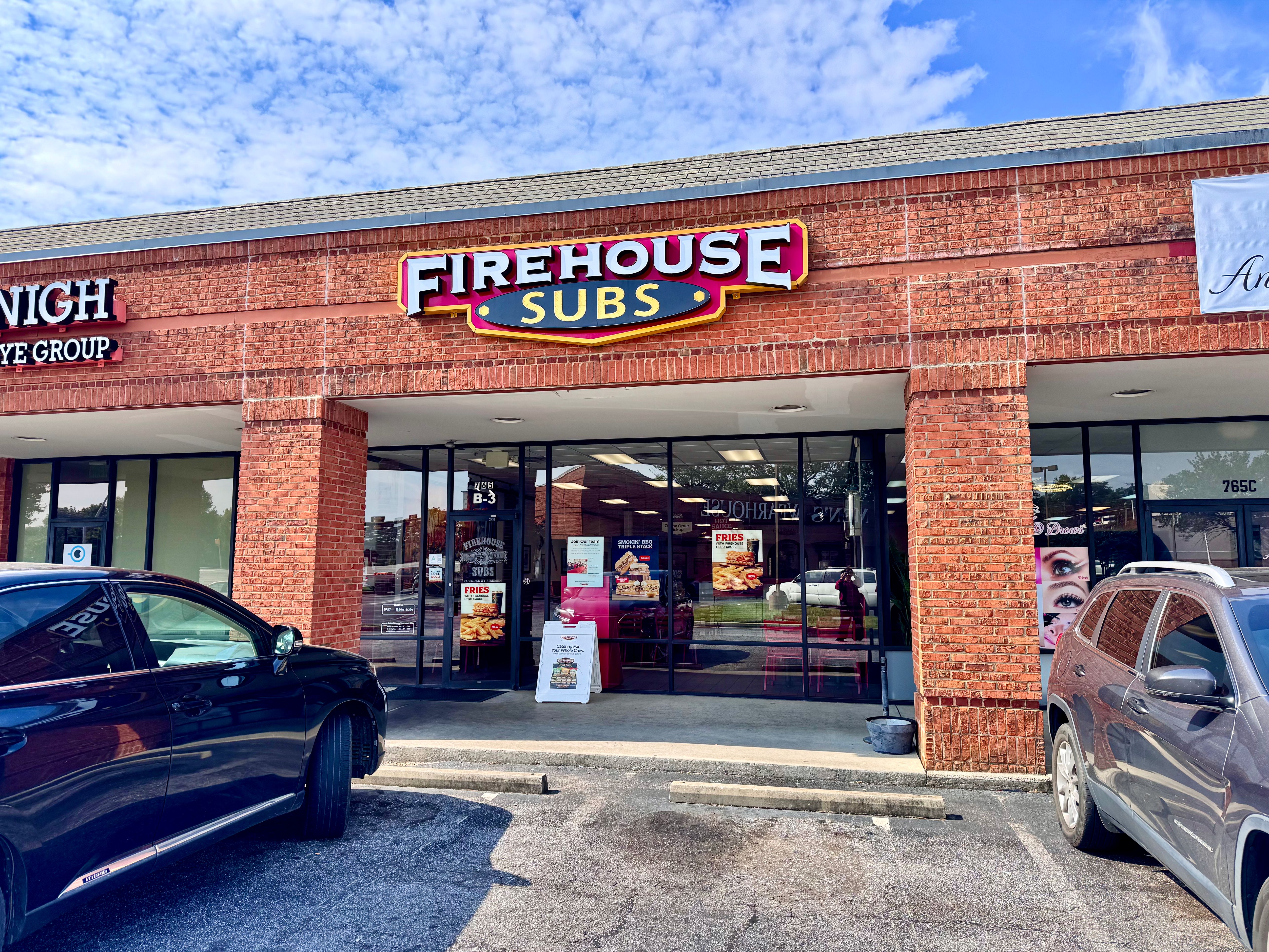 Firehouse Subs storefront in a brick strip mall with illuminated sign above entrance.