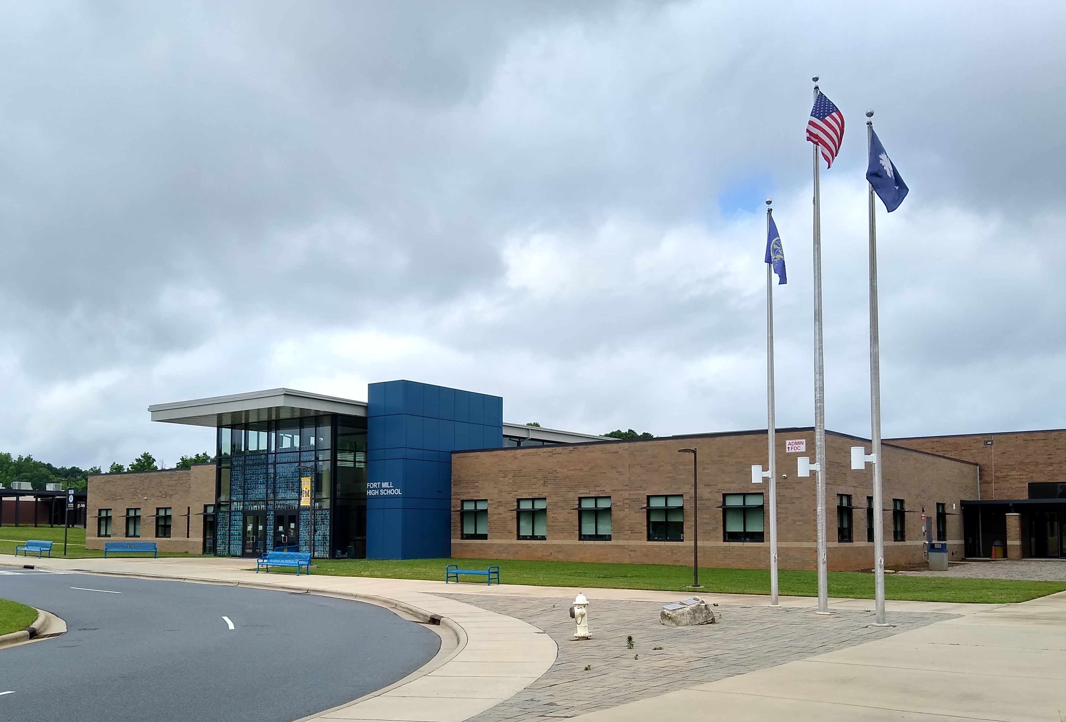 Brick school building with three flagpoles and a curved driveway under overcast skies.