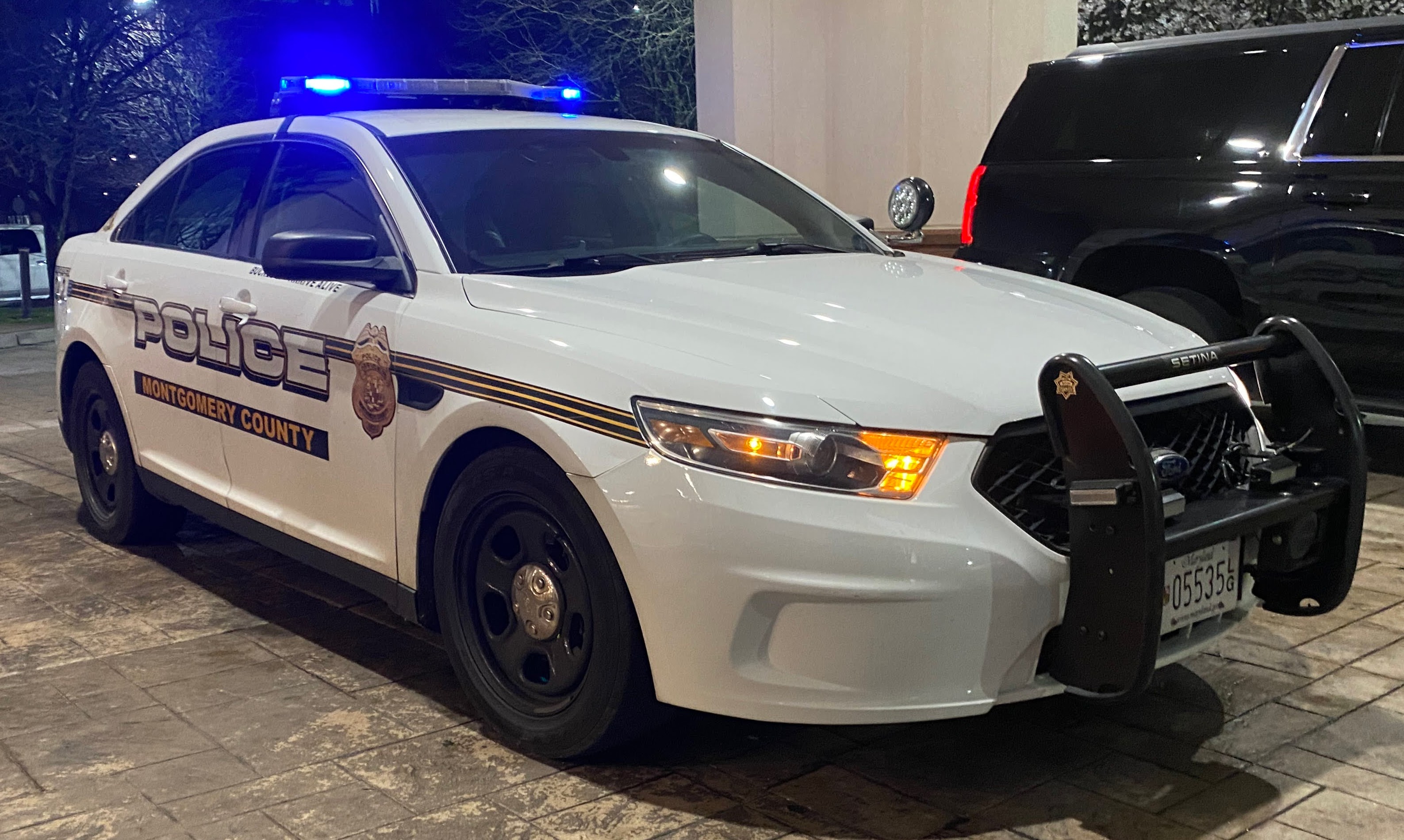 White police patrol car with blue emergency lights flashing at night.