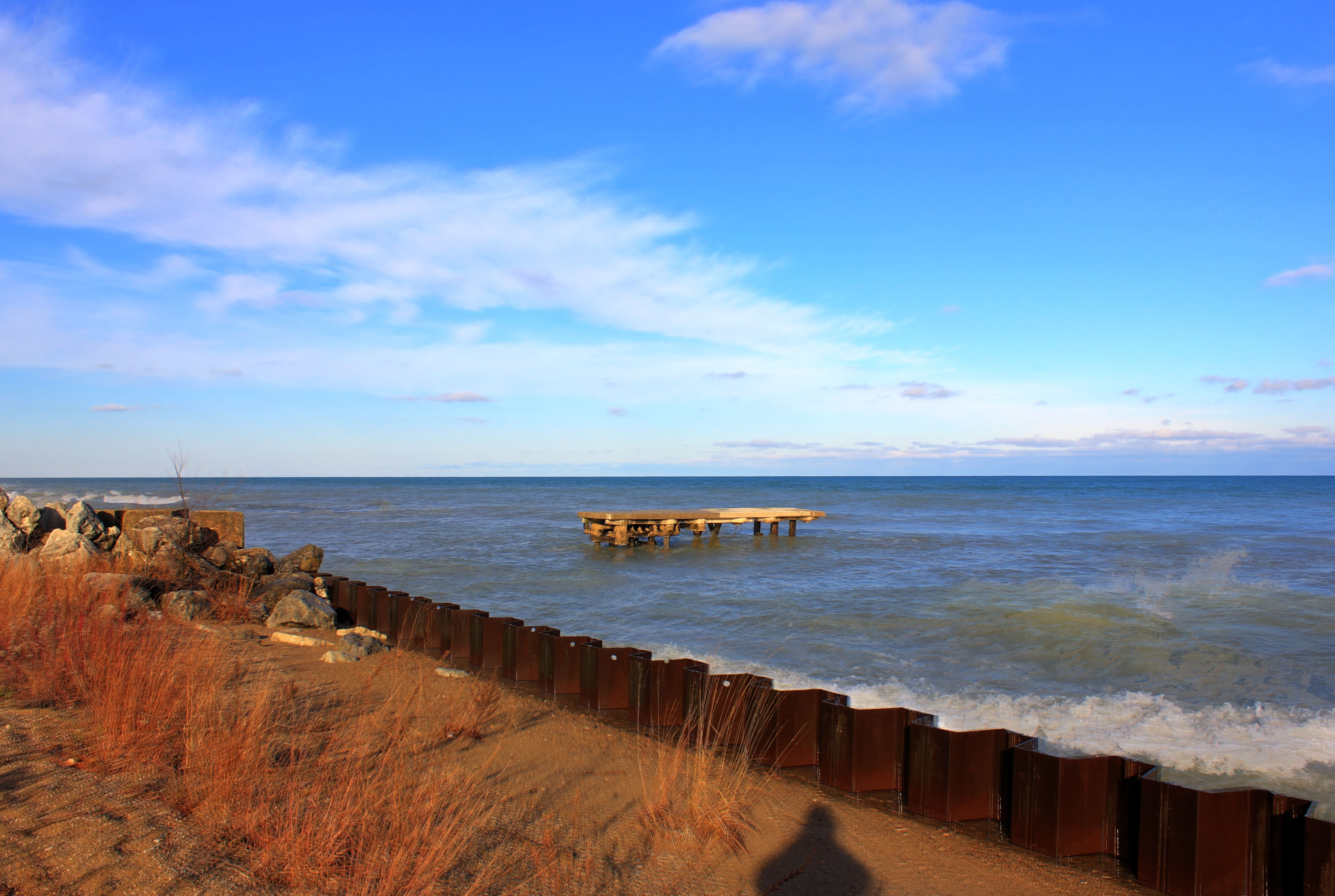 Rocky Lake Michigan shoreline with a steel retaining wall and deteriorating pier structure.