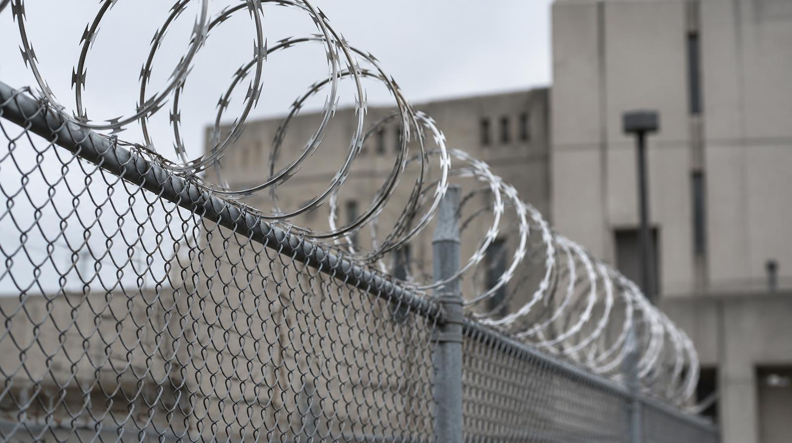 Chain-link fence with coiled razor wire in front of a concrete building.