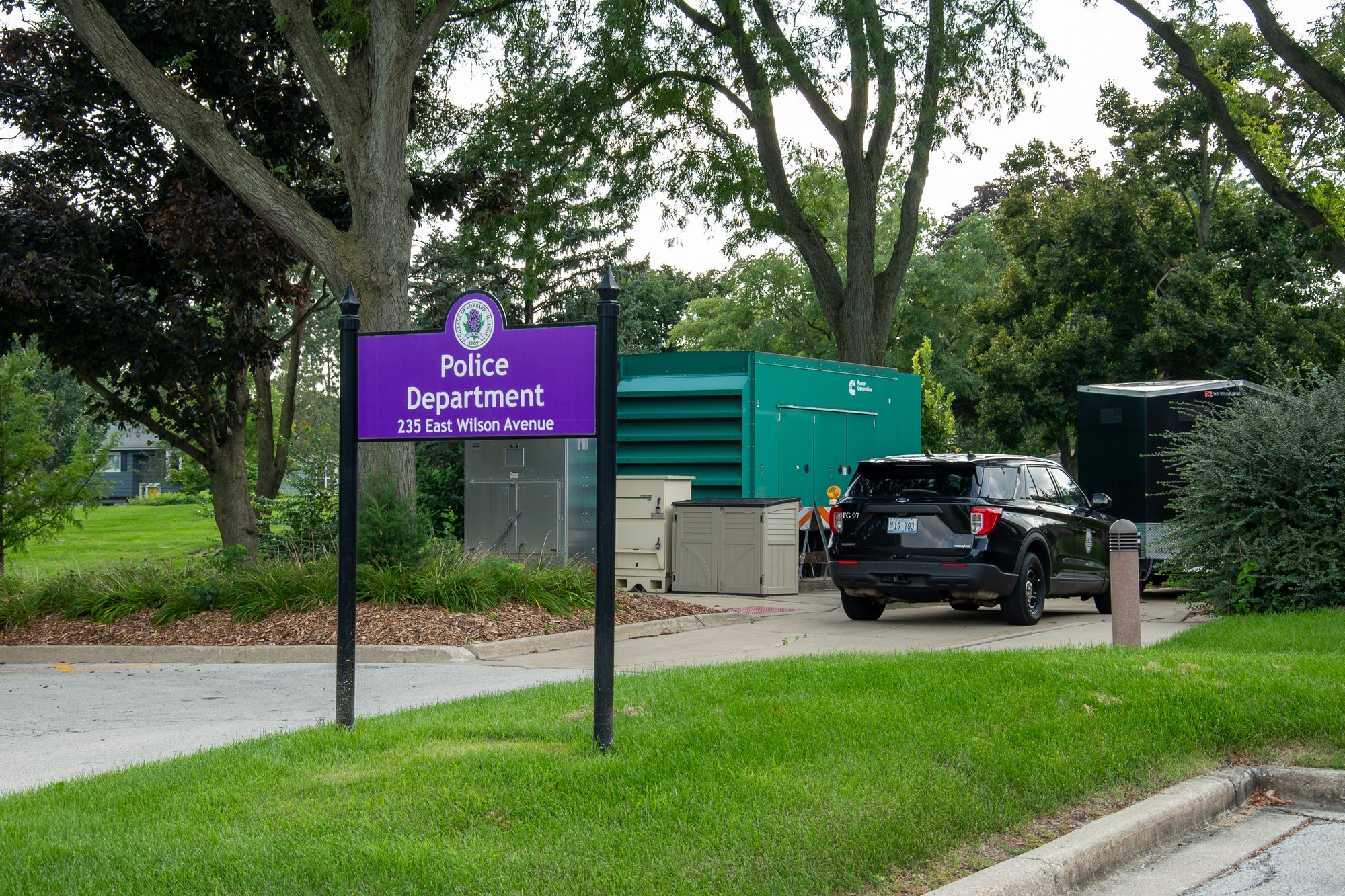 Purple police department sign at station entrance with parked SUV behind it.