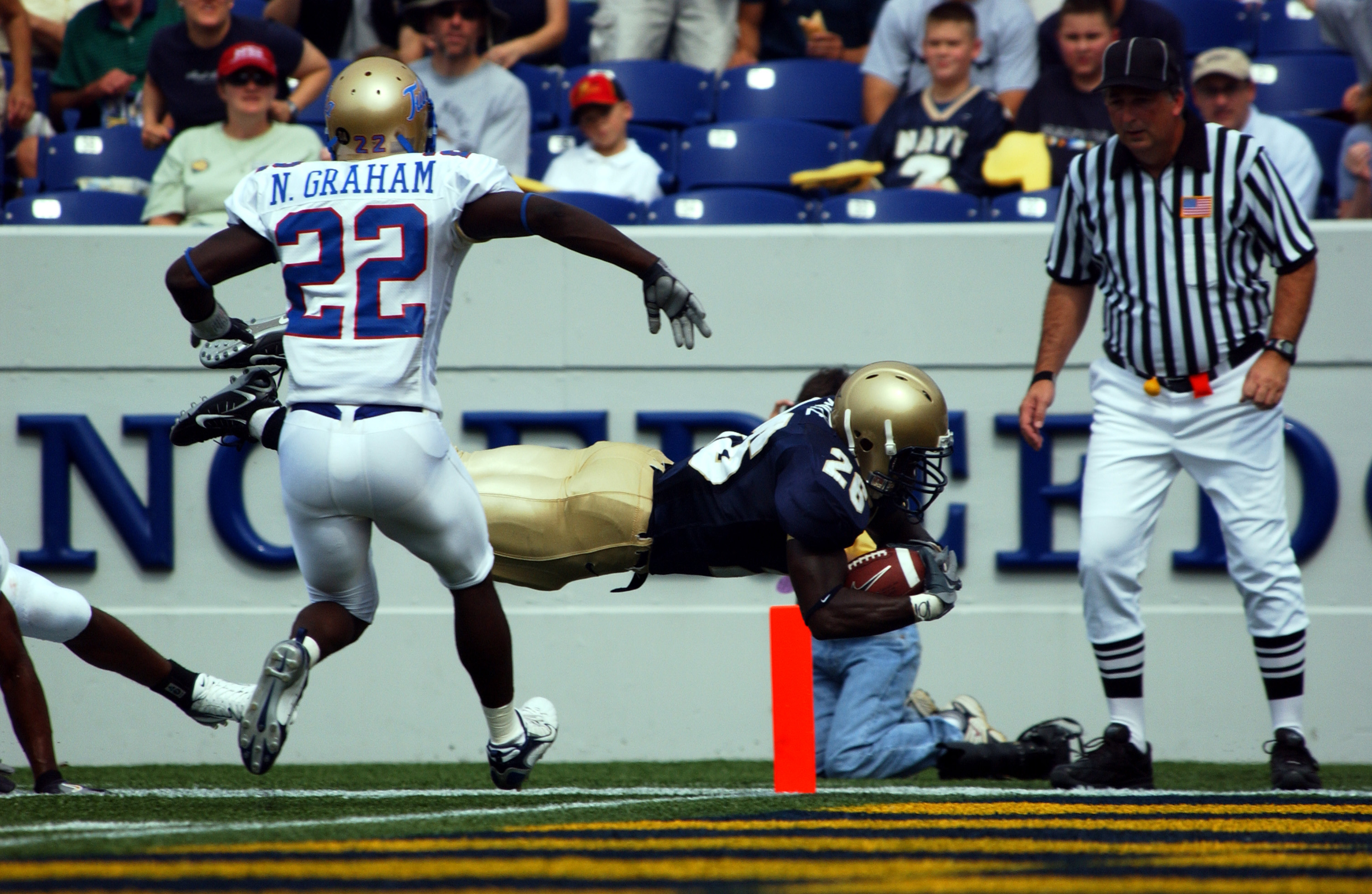A football player in a dark uniform dives toward the end zone pylon.