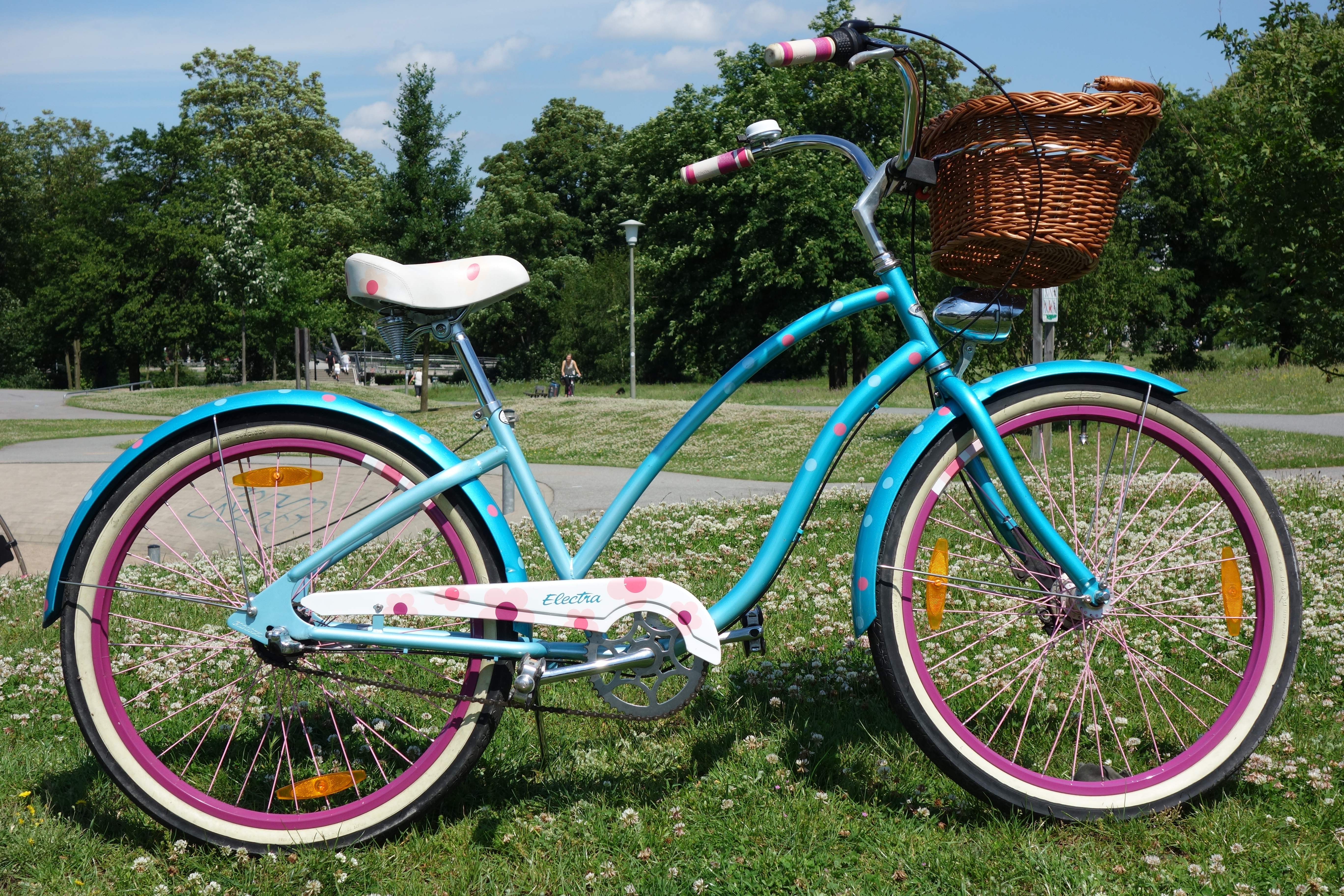 Turquoise Electra brand beach cruiser bicycle with pink rims and wicker basket.
