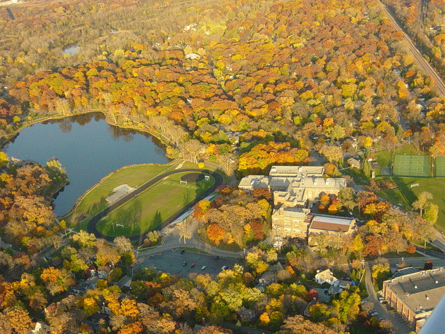 Aerial view of a lake and school campus surrounded by autumn foliage in orange and red.