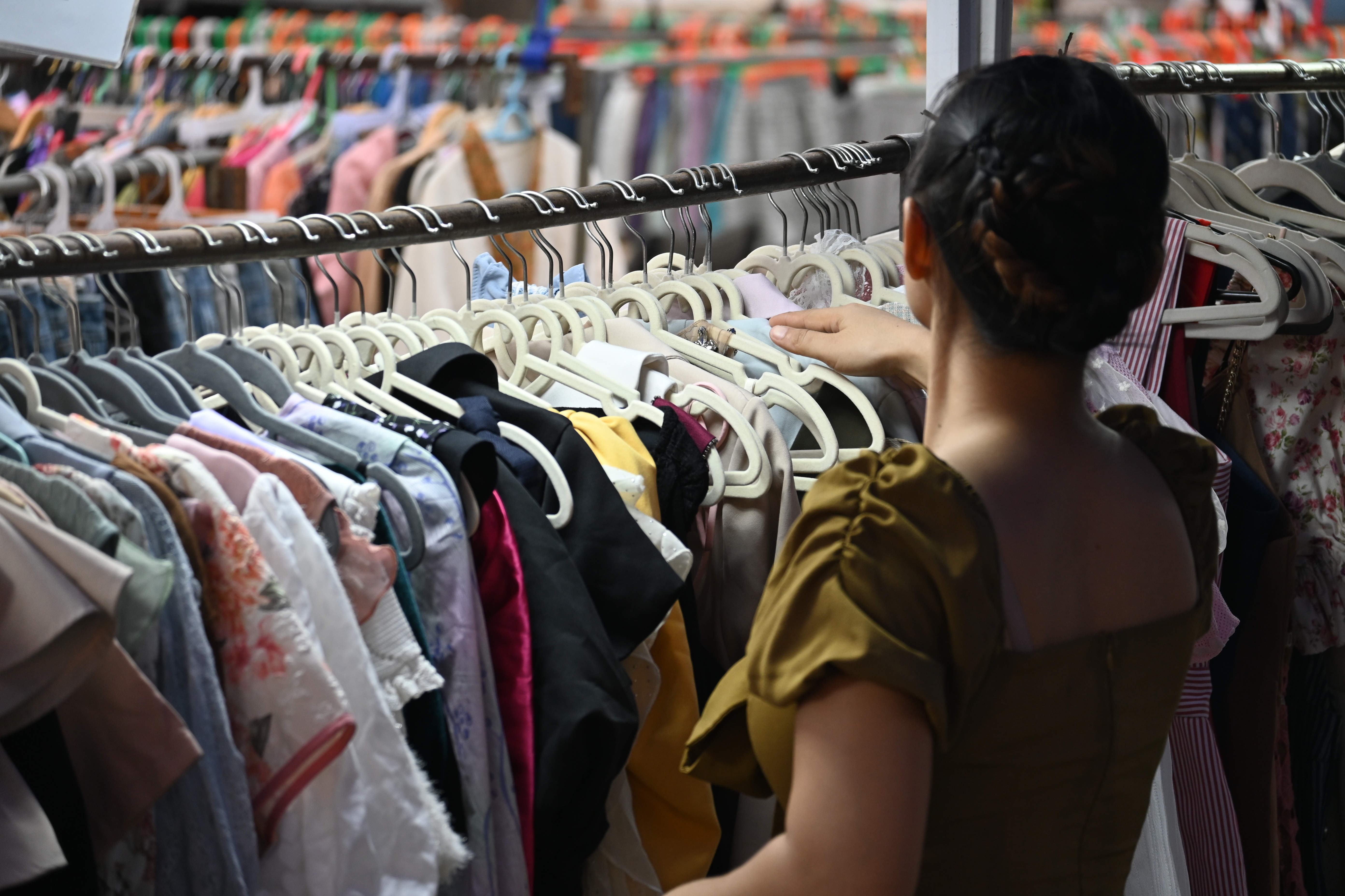 A shopper seen from behind browses a crowded rack of colorful clothing.