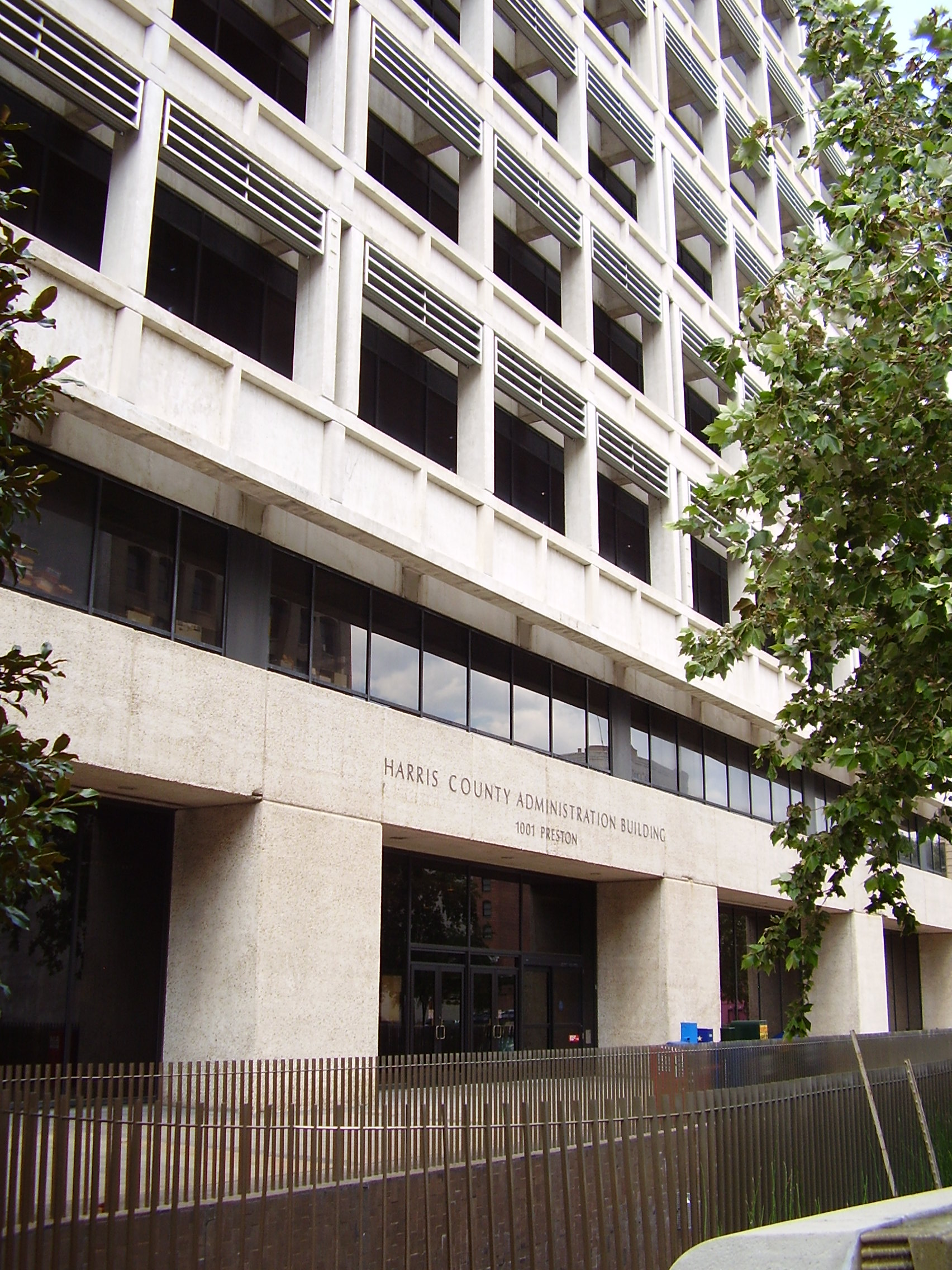 Exterior of a multi-story modernist concrete government building with a metal fence.