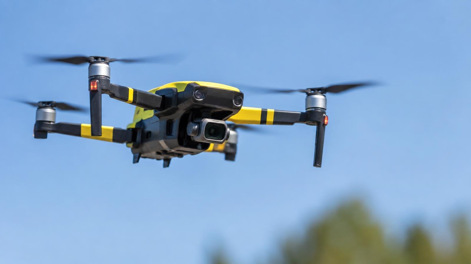 Small quadcopter drone hovering against a clear blue sky.