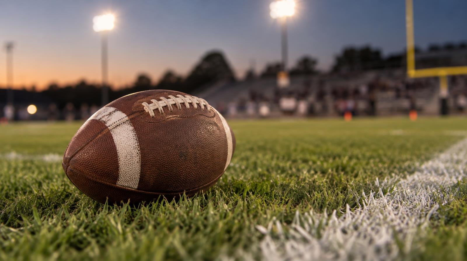 An American football resting on green grass beside a white painted yard line.