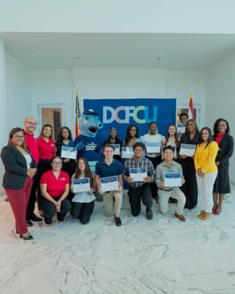 Group of students holding certificates posing with staff in front of a DCFCU banner.