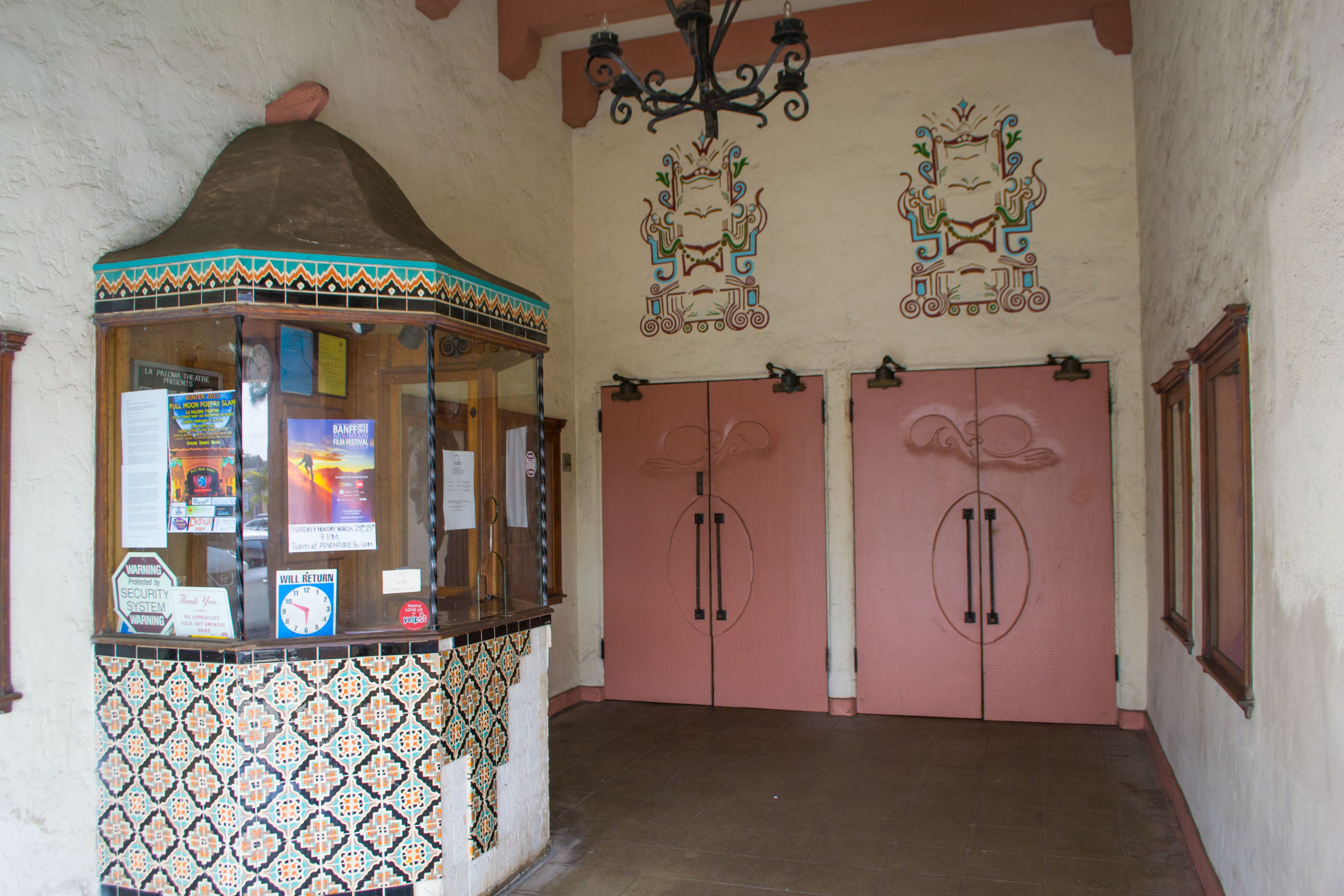 Ornate theatre entrance with tiled booth, pink double doors, and painted murals.