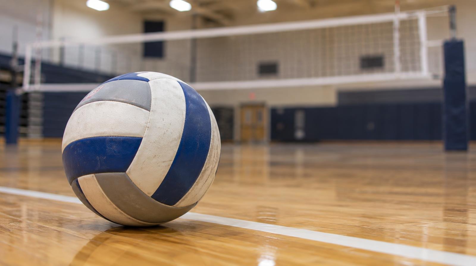 A volleyball rests on a hardwood gym floor beside a white boundary line.