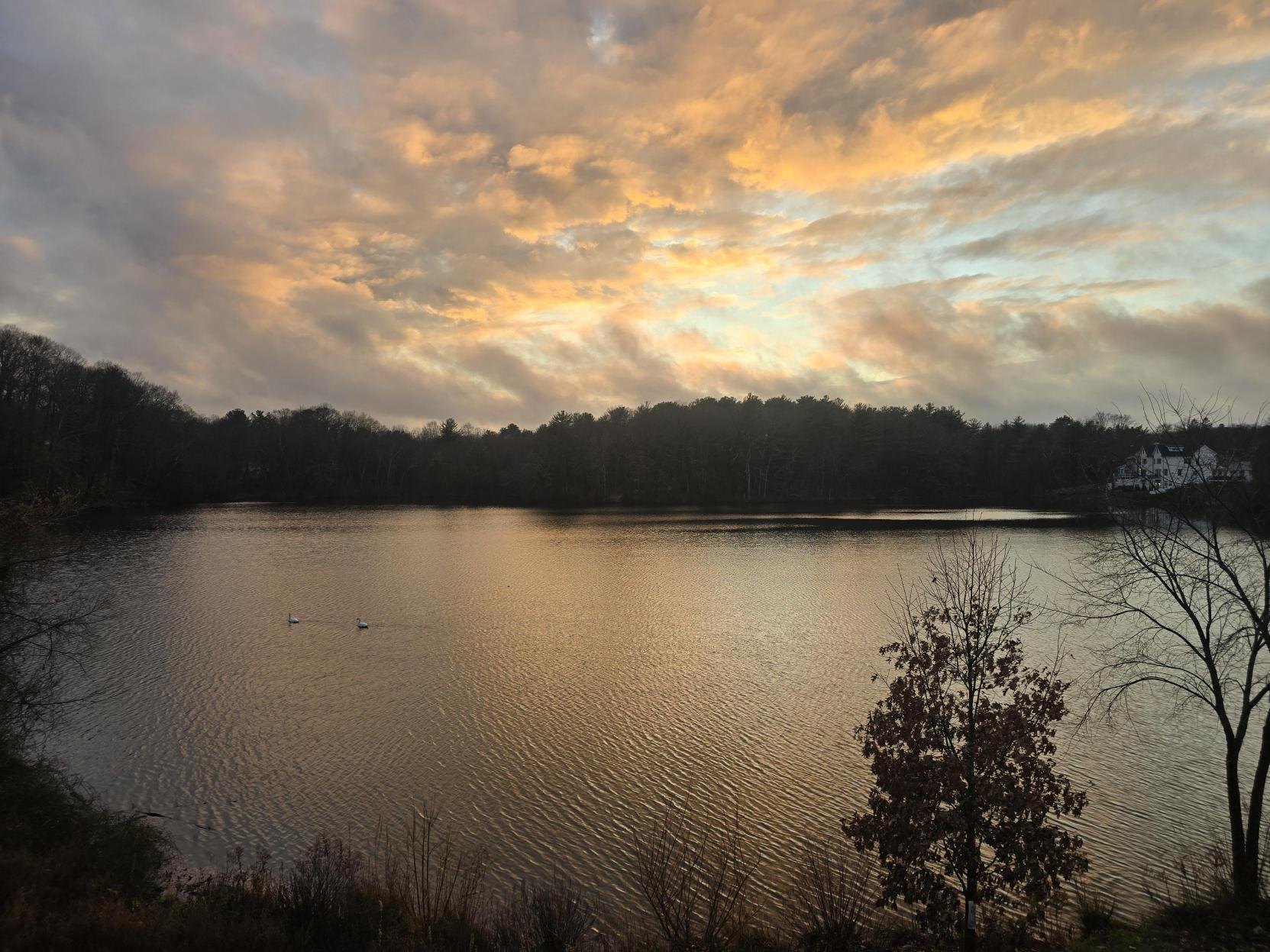 A calm lake at dusk with an orange-tinted sky reflected on the rippled water surface.