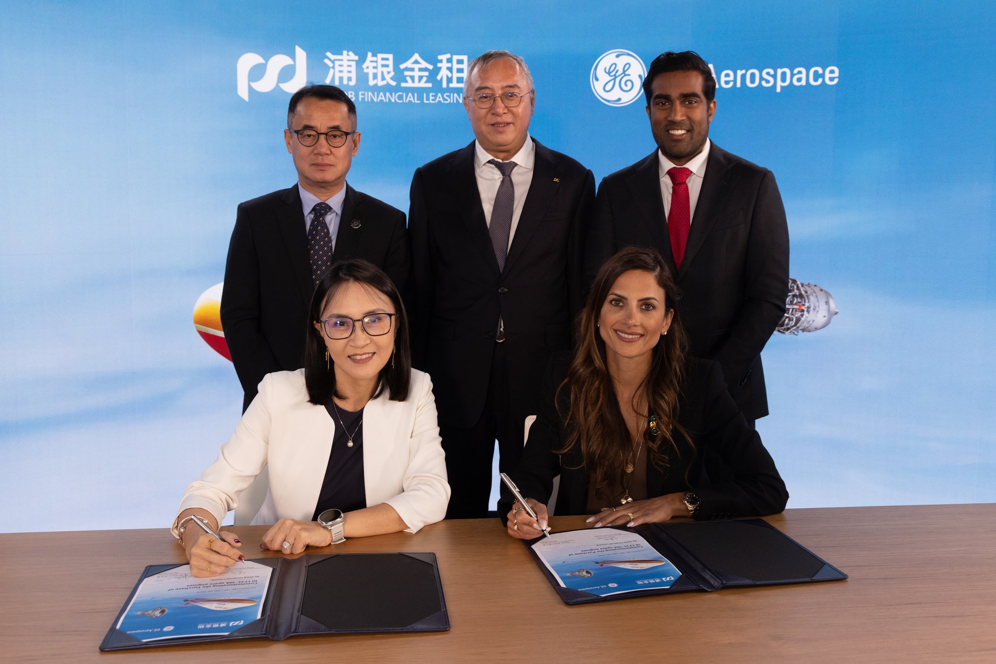 Two women sign documents at a table beneath GE Aerospace and SPDB Financial Leasing logos.