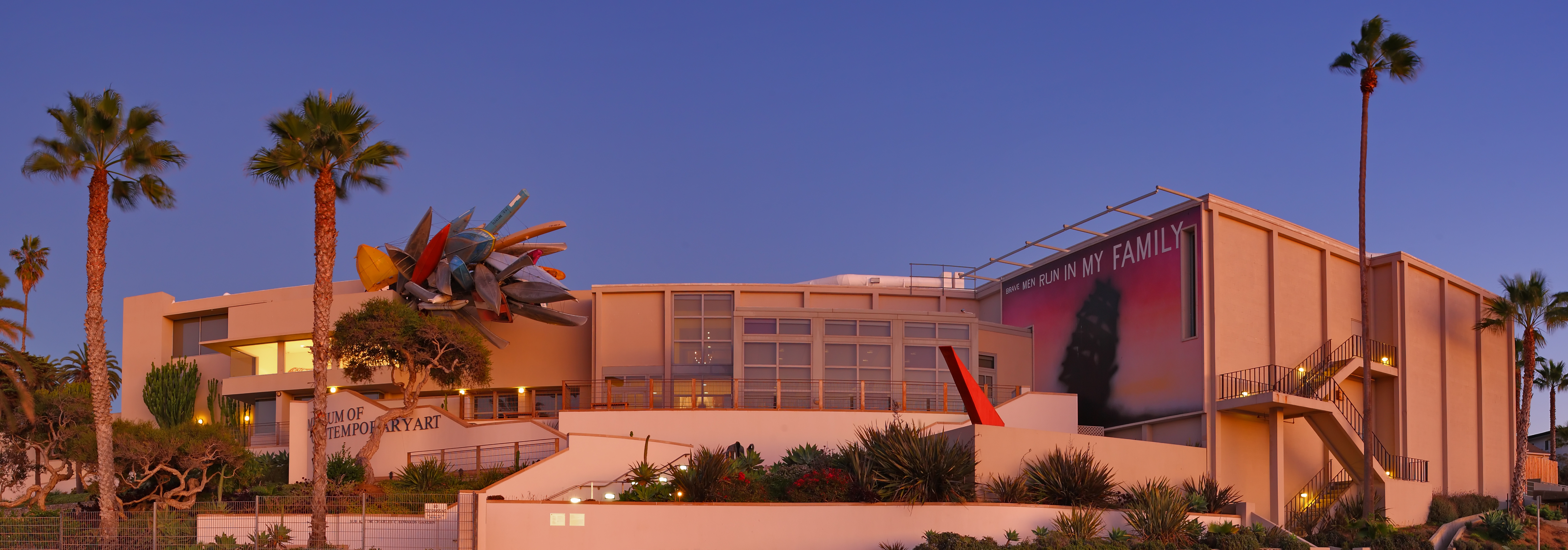 White modernist museum building at dusk surrounded by palm trees against a twilight sky.