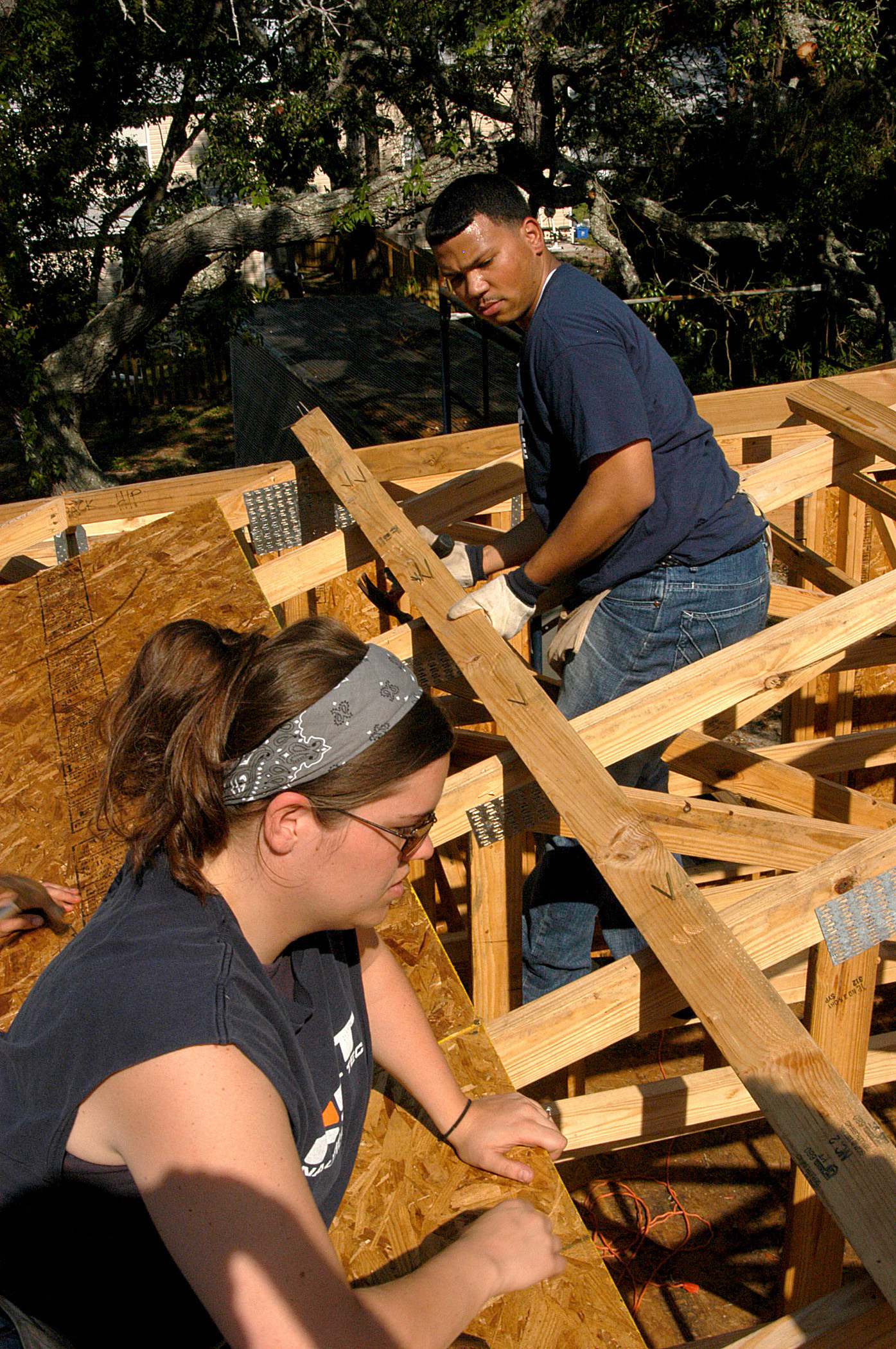 Two volunteers frame a wooden house structure at an outdoor Beaches Habitat construction site.