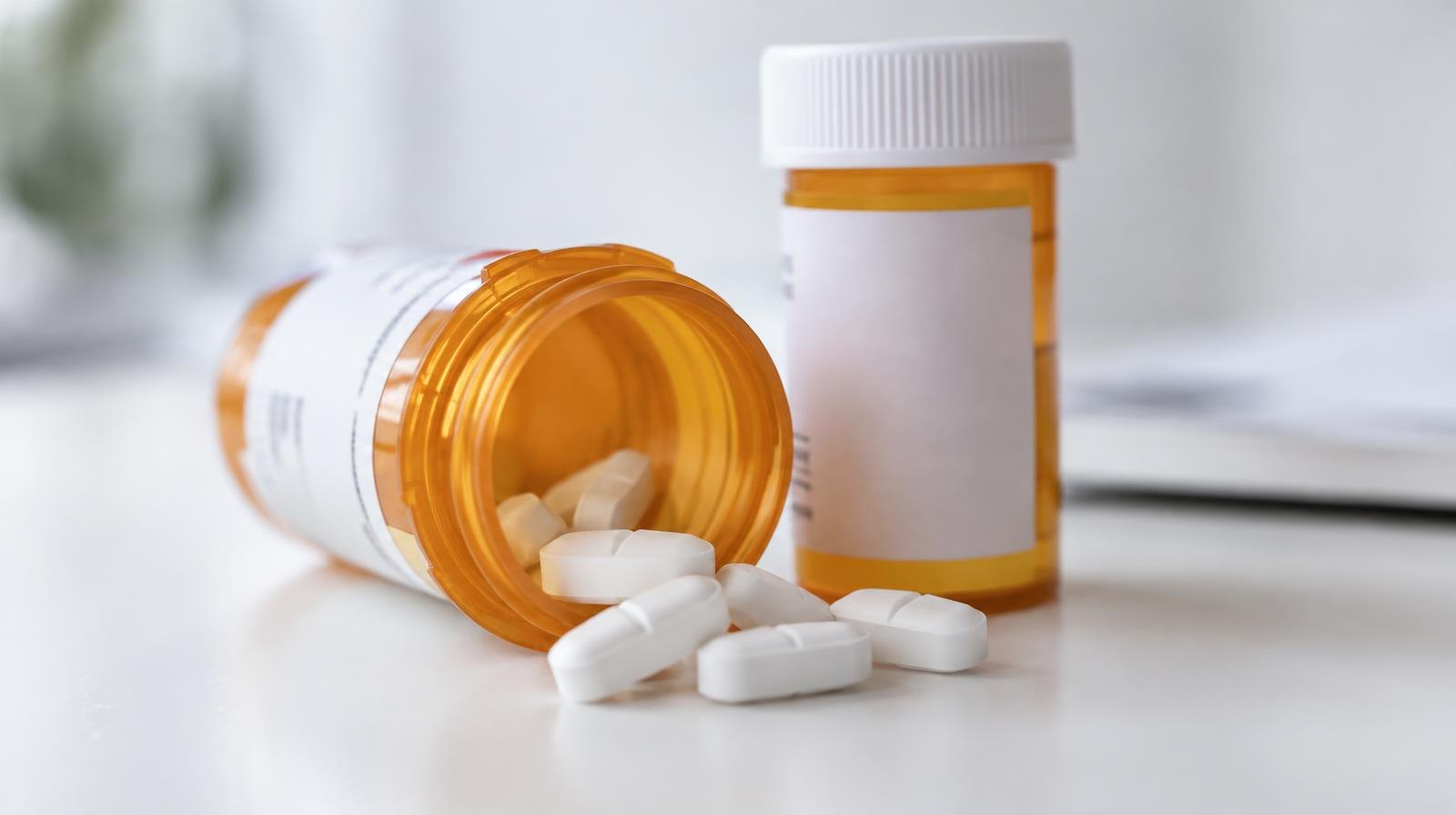 Amber prescription pill bottle on its side with white tablets spilling onto a white surface.
