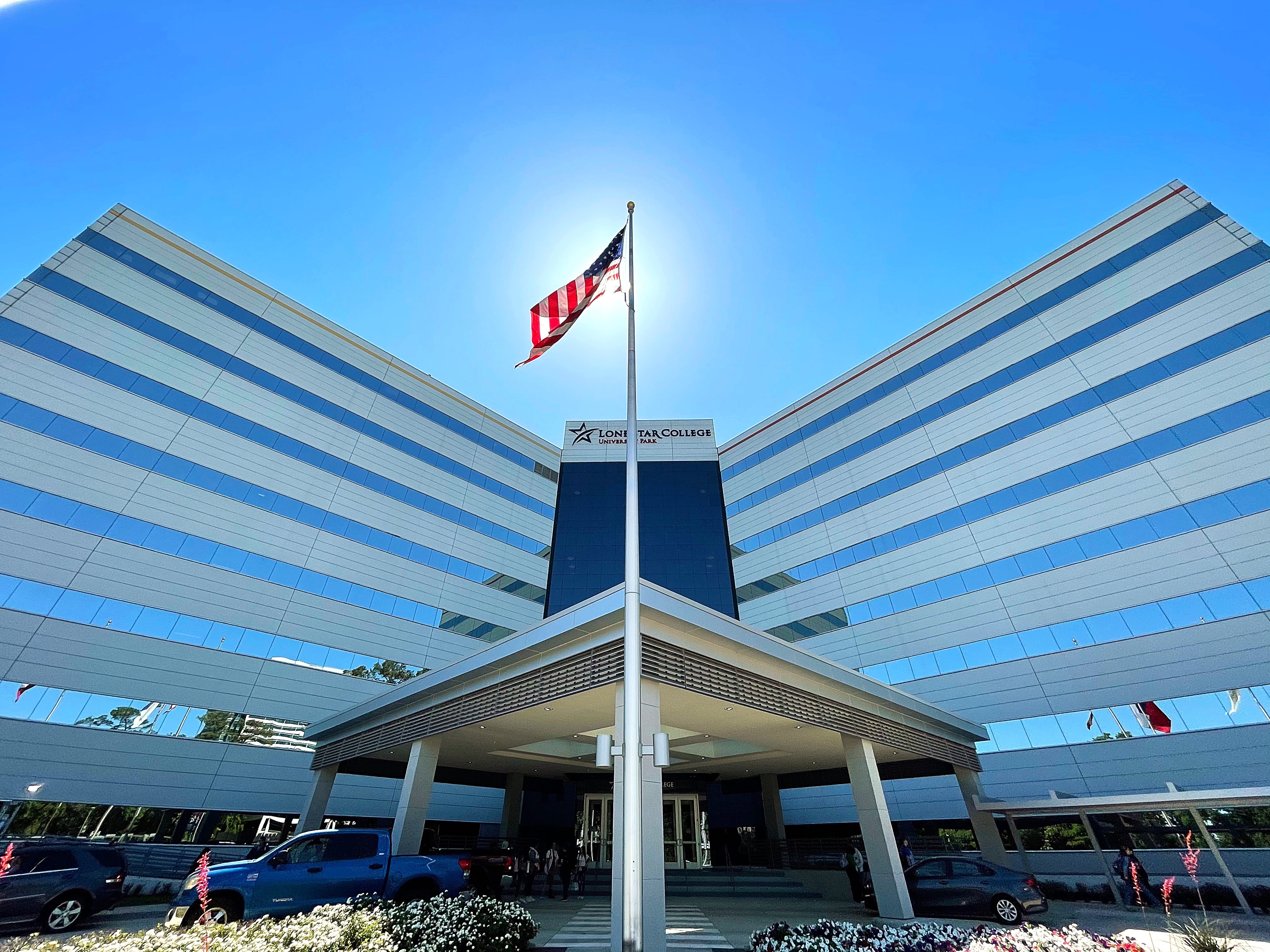 Wide exterior view of a Lone Star College building with flagpole and glass-and-steel entrance canopy.