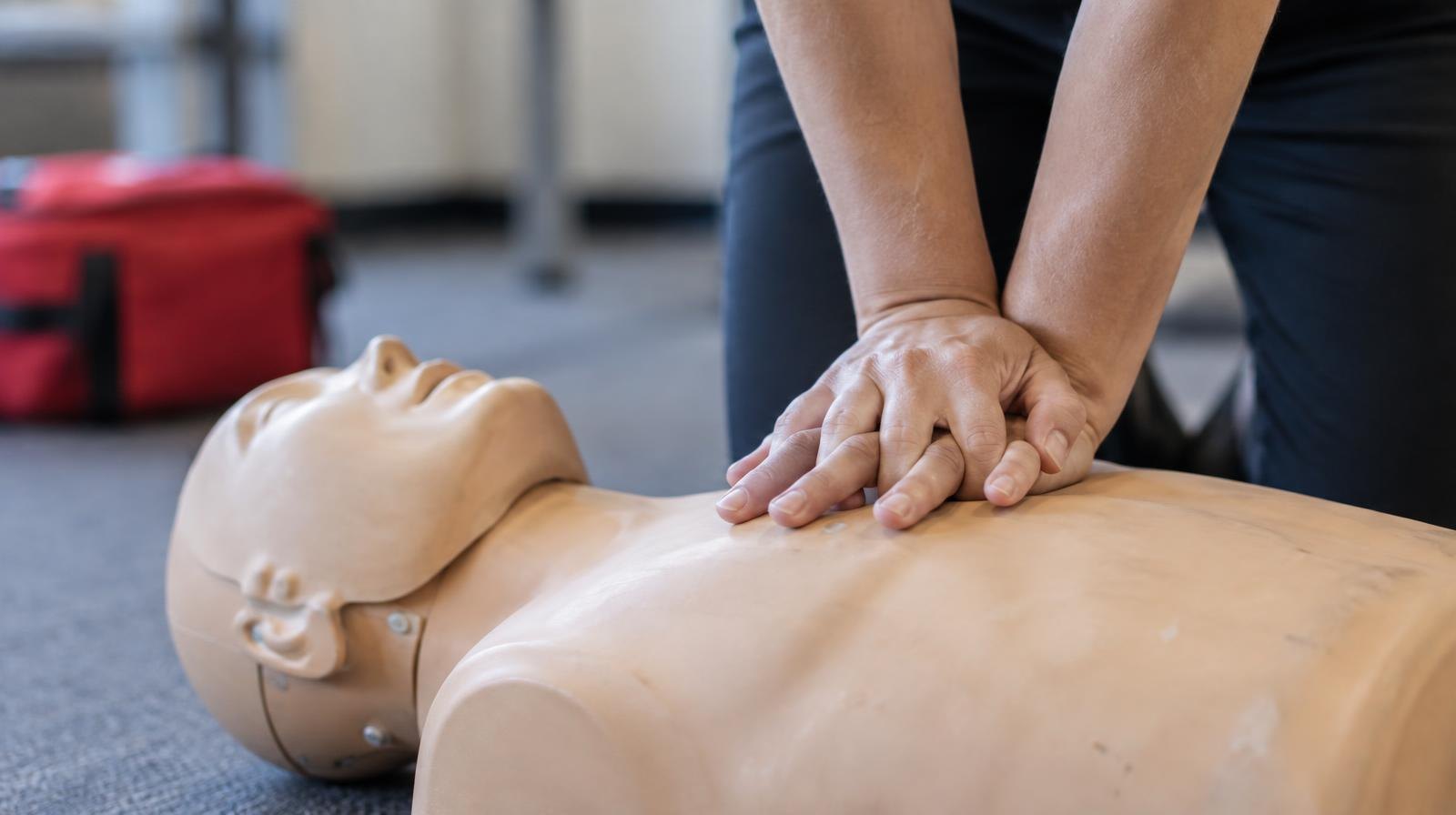 Two hands pressing down on a CPR training mannequin on a flat surface.