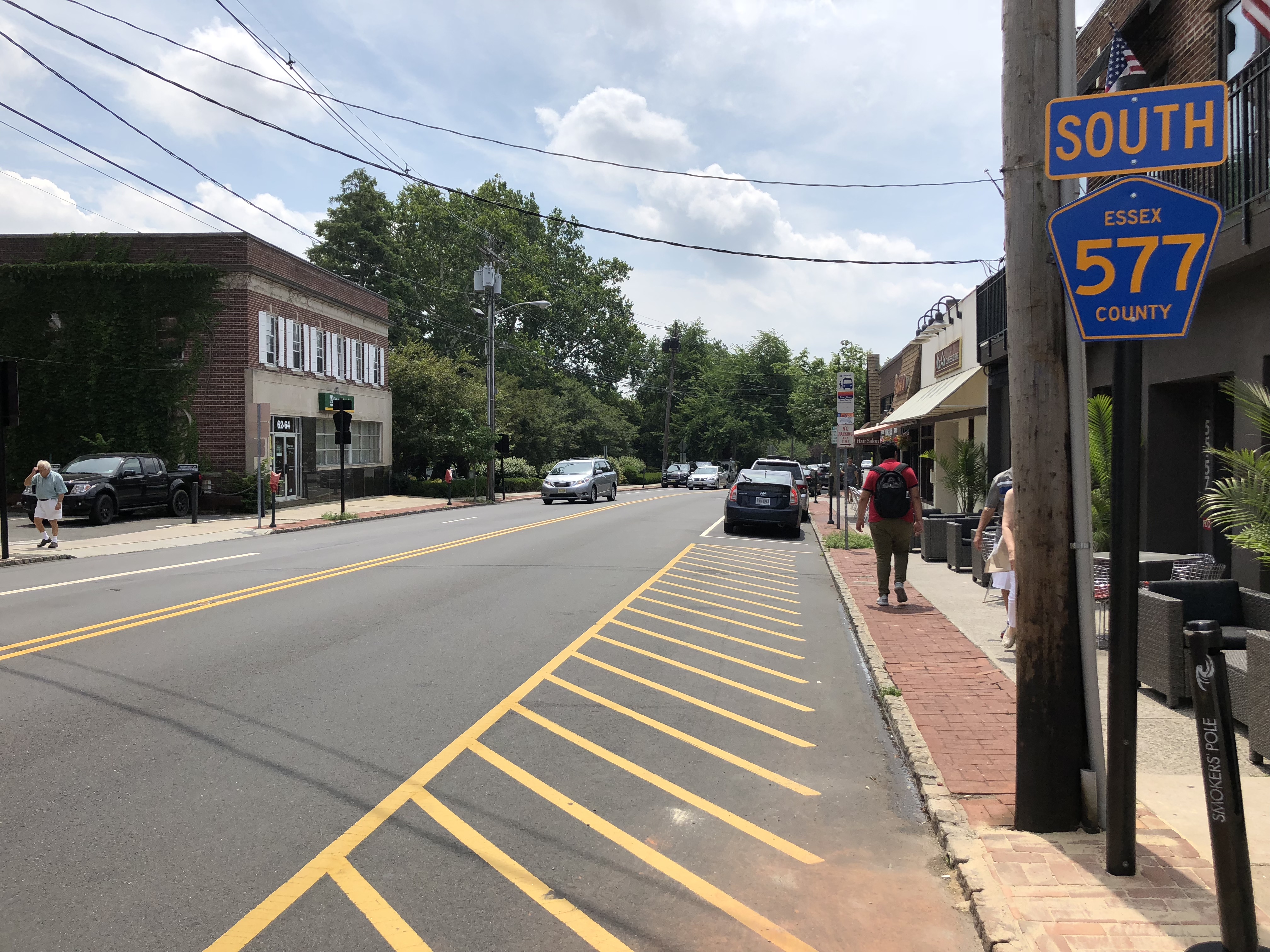 View south along Main Street in Millburn showing storefronts, brick sidewalks, and road markings.