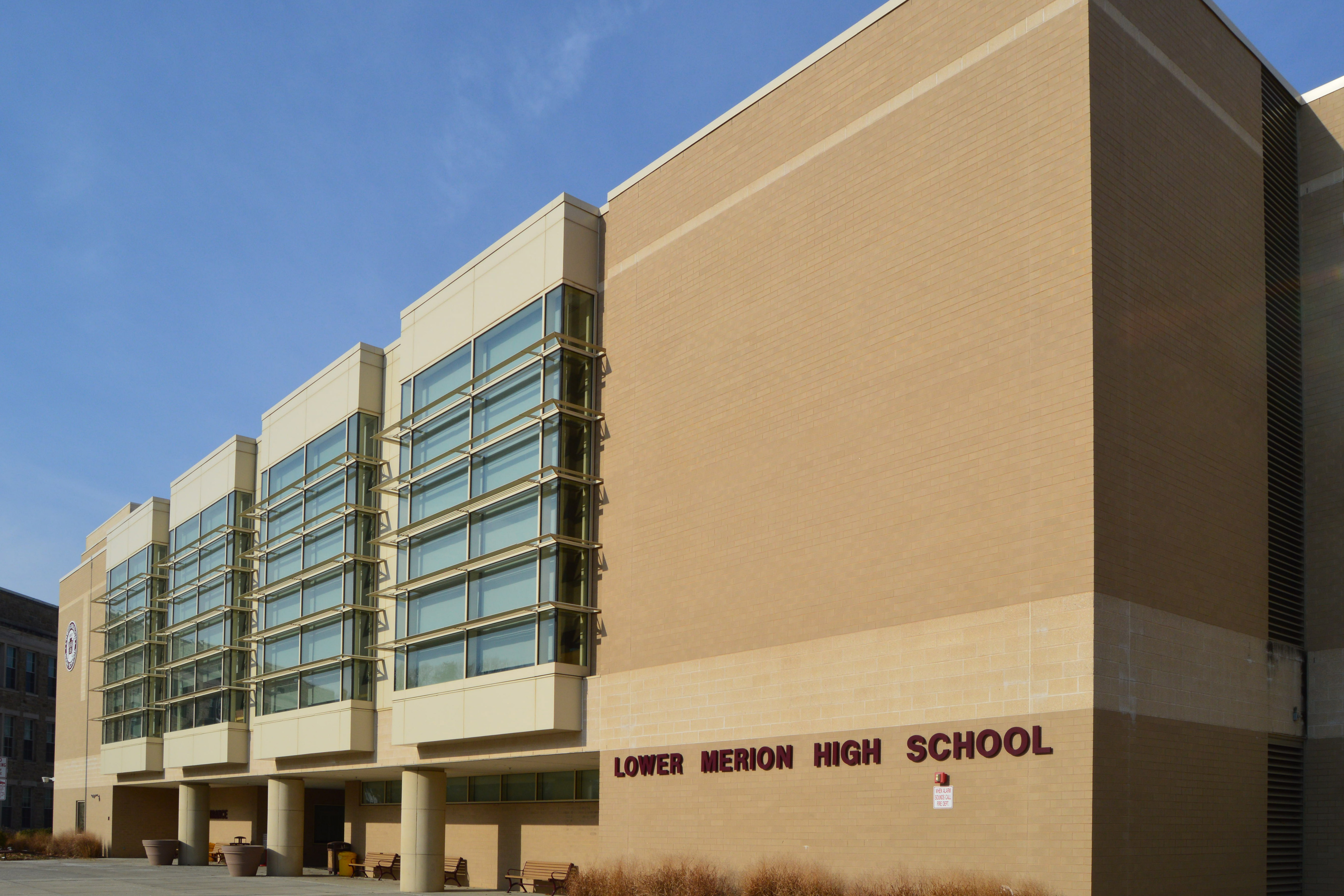 Exterior of a large brick high school building with a parking area in front.