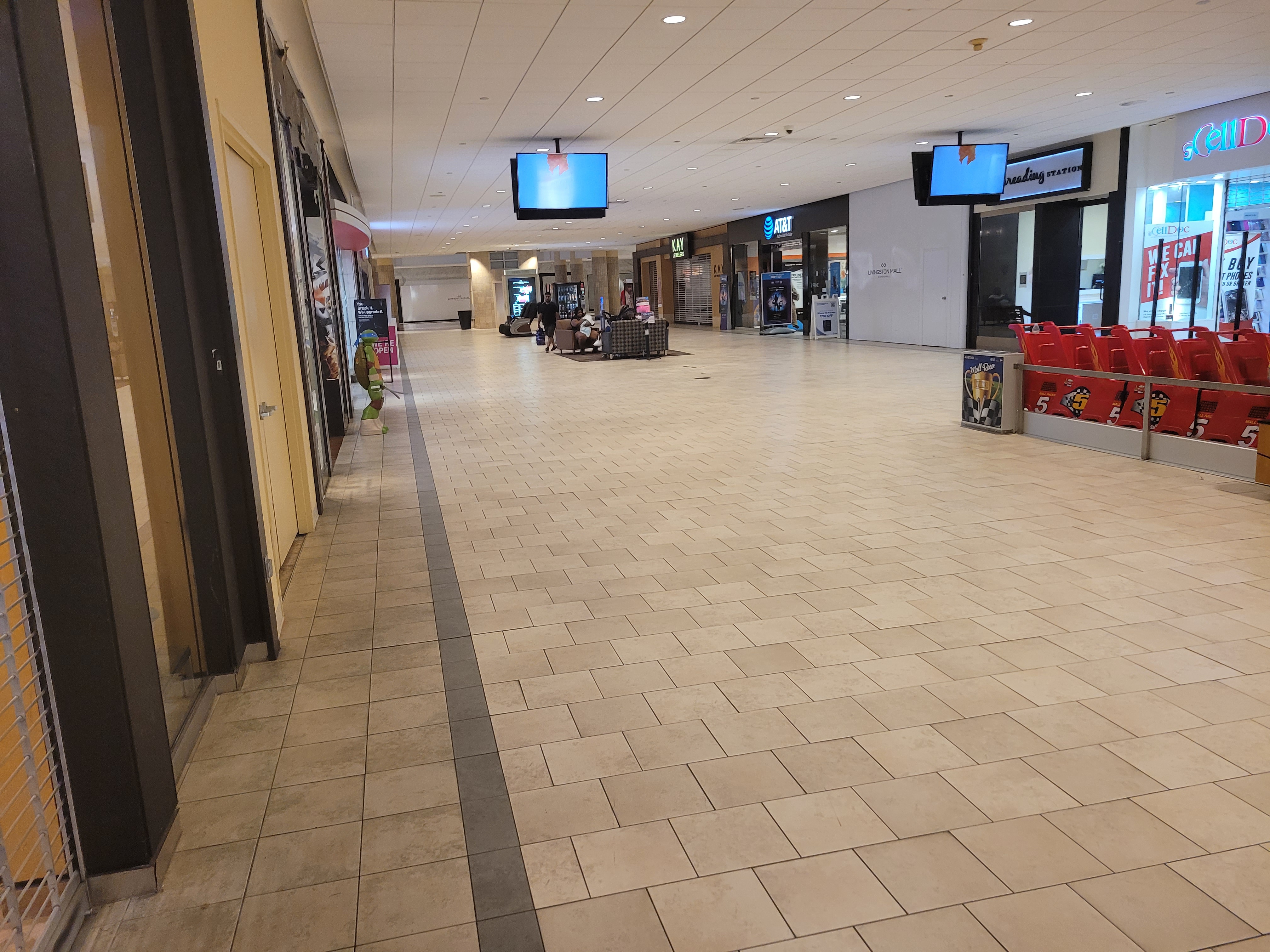 Wide, mostly empty mall corridor with some dark storefronts and red seating along one side.