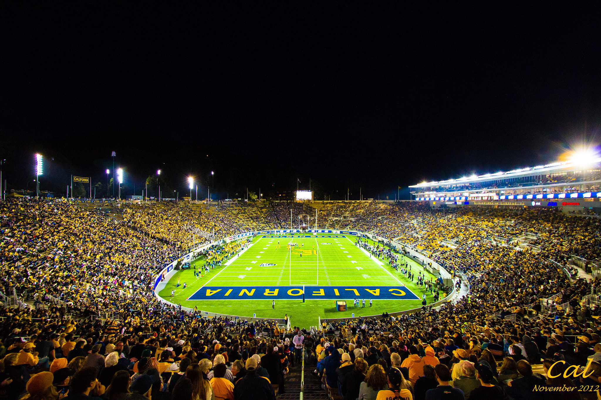 Packed football stadium at night with the field illuminated and 'CALIFORNIA' on the turf.