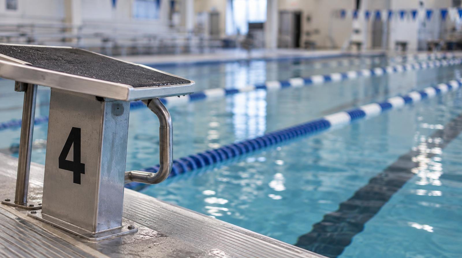 An indoor pool lane with a starting block at the edge and lane dividers stretching into the distance.
