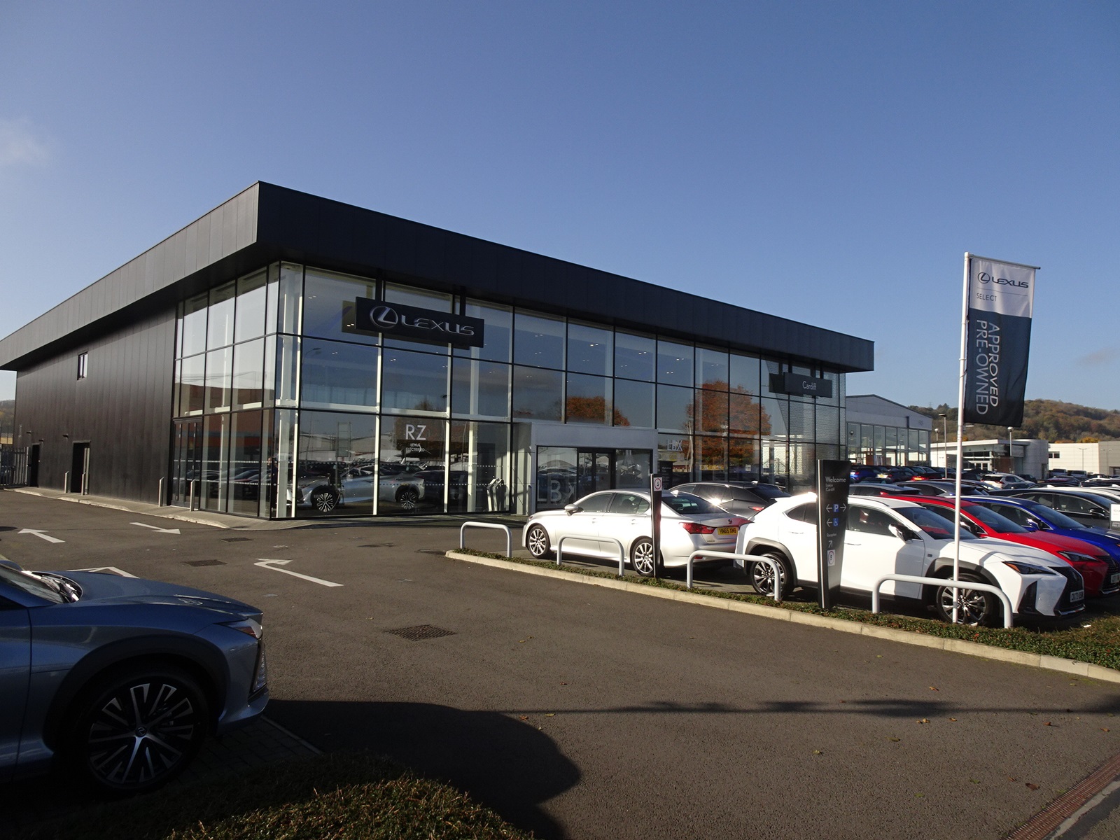 Modern Lexus dealership building with large glass windows, brand logo, and cars parked outside.