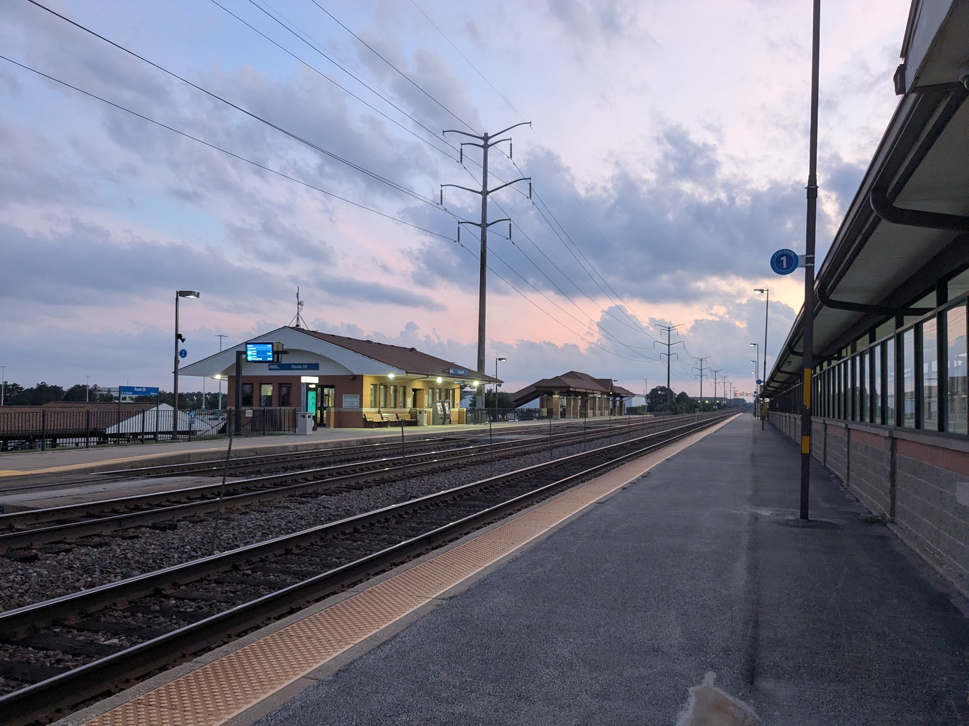 Commuter rail tracks and covered platform at the Route 59 Metra station at dusk.