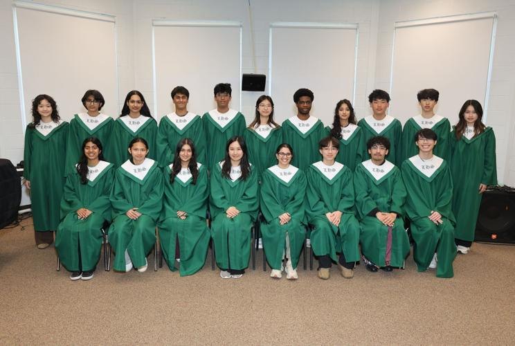 Group of approximately 20 students in green choir robes with white stoles posed in two rows indoors.