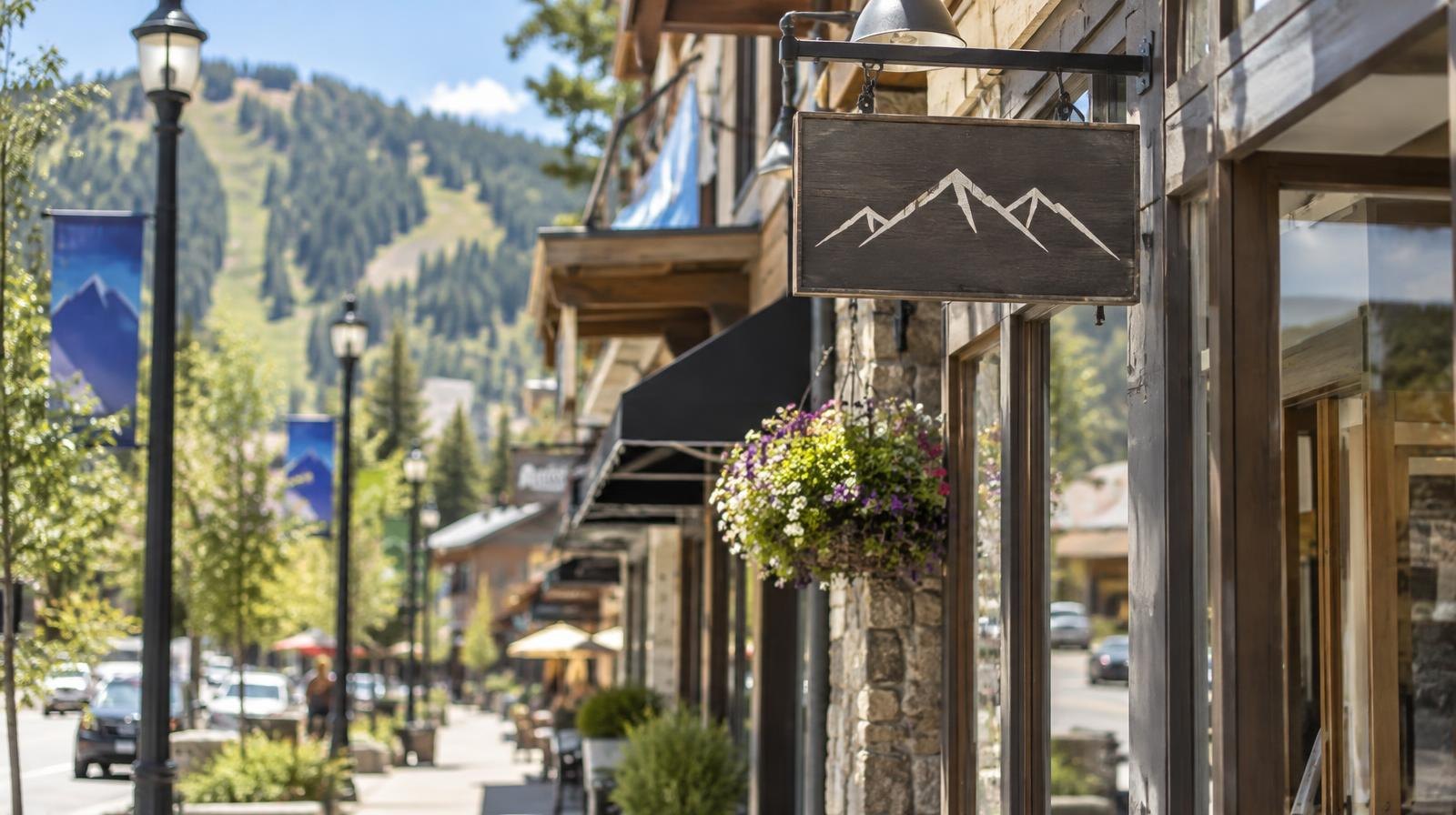 Row of retail storefronts with banners along a mountain-town street under a clear sky.