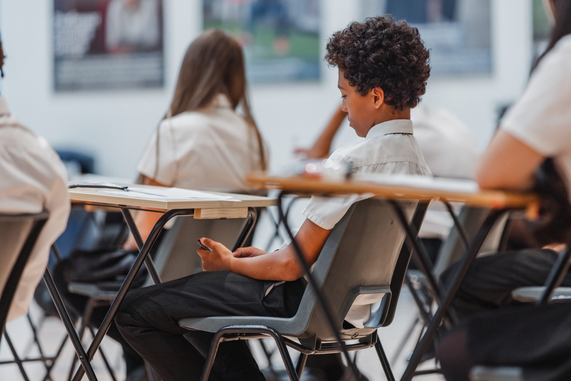 Young male student checking his phone in a classroom photographed at a British high school, Kenton, Newcastle upon Tyne, England, United Kingdom