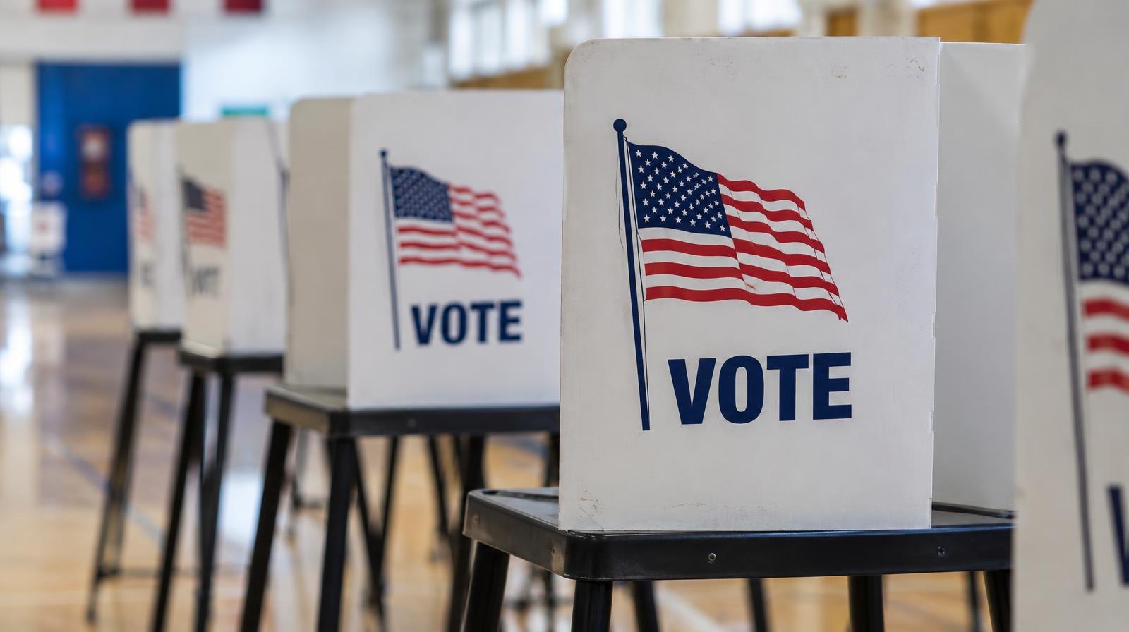 A row of official-style voting booths with privacy screens in a bright indoor space.