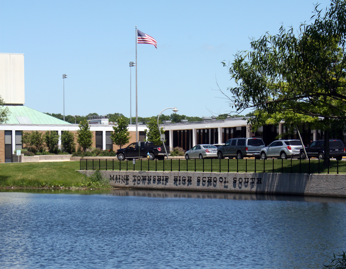 Exterior of a high school building with a pond in the foreground and an American flag on a flagpole.