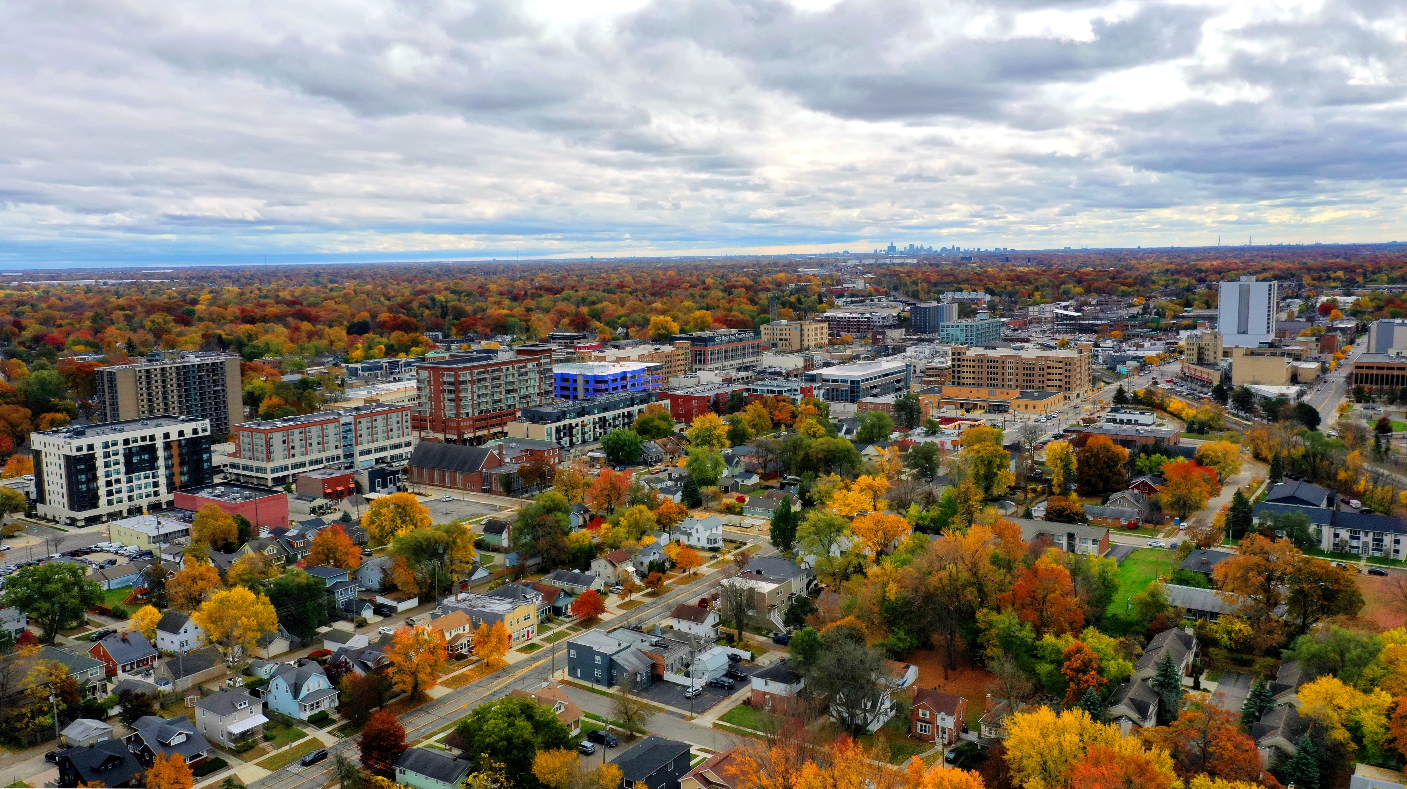 Aerial view of houses, downtown buildings and trees with colorful fall foliage beneath a cloudy sky.