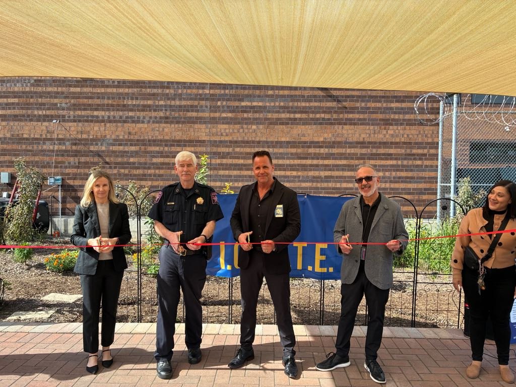Five people cut a red ribbon in front of a blue I.G.N.I.T.E. banner at a jail facility.