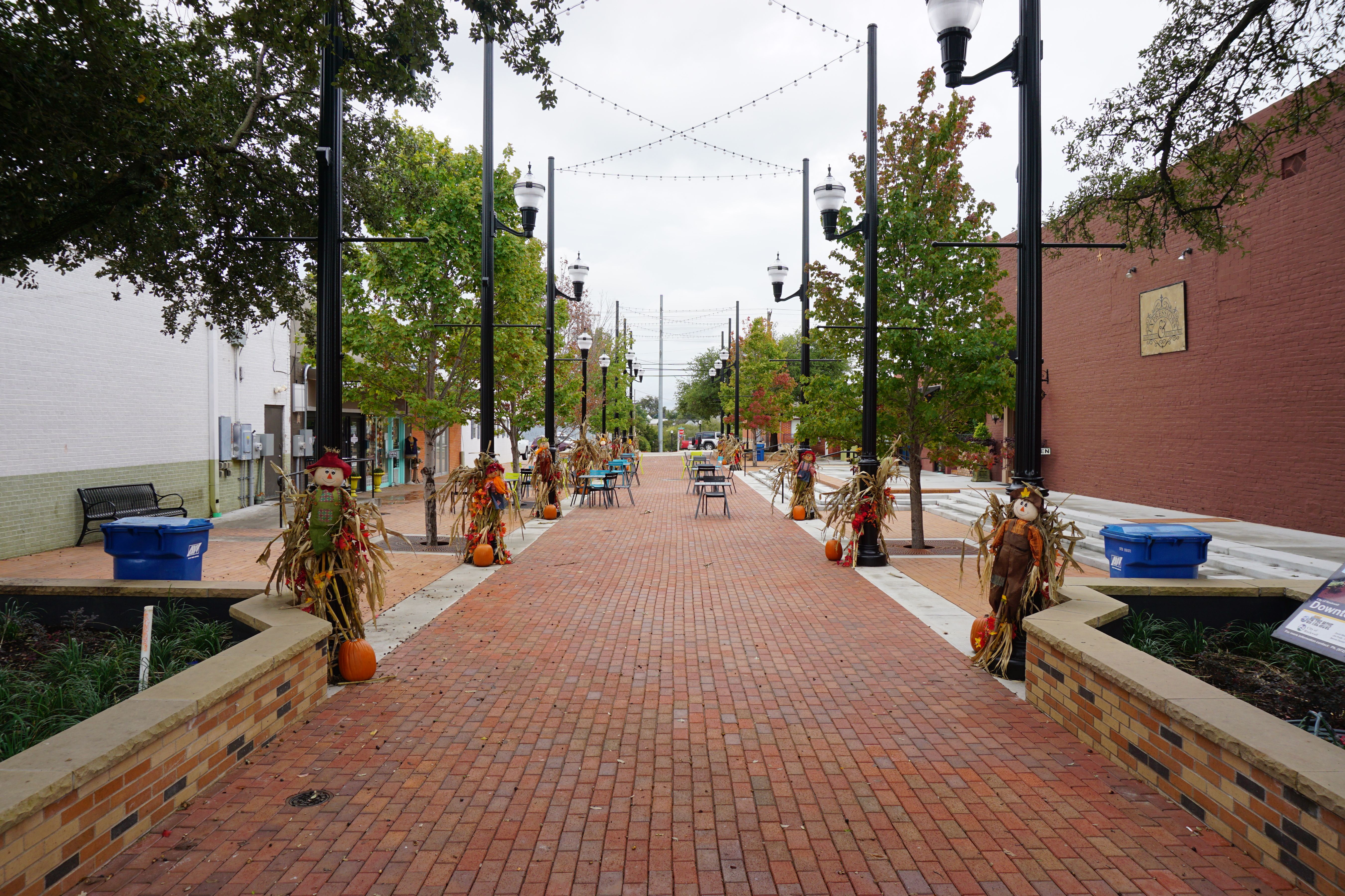 Brick pedestrian plaza lined with lamp posts and string lights in a small town.