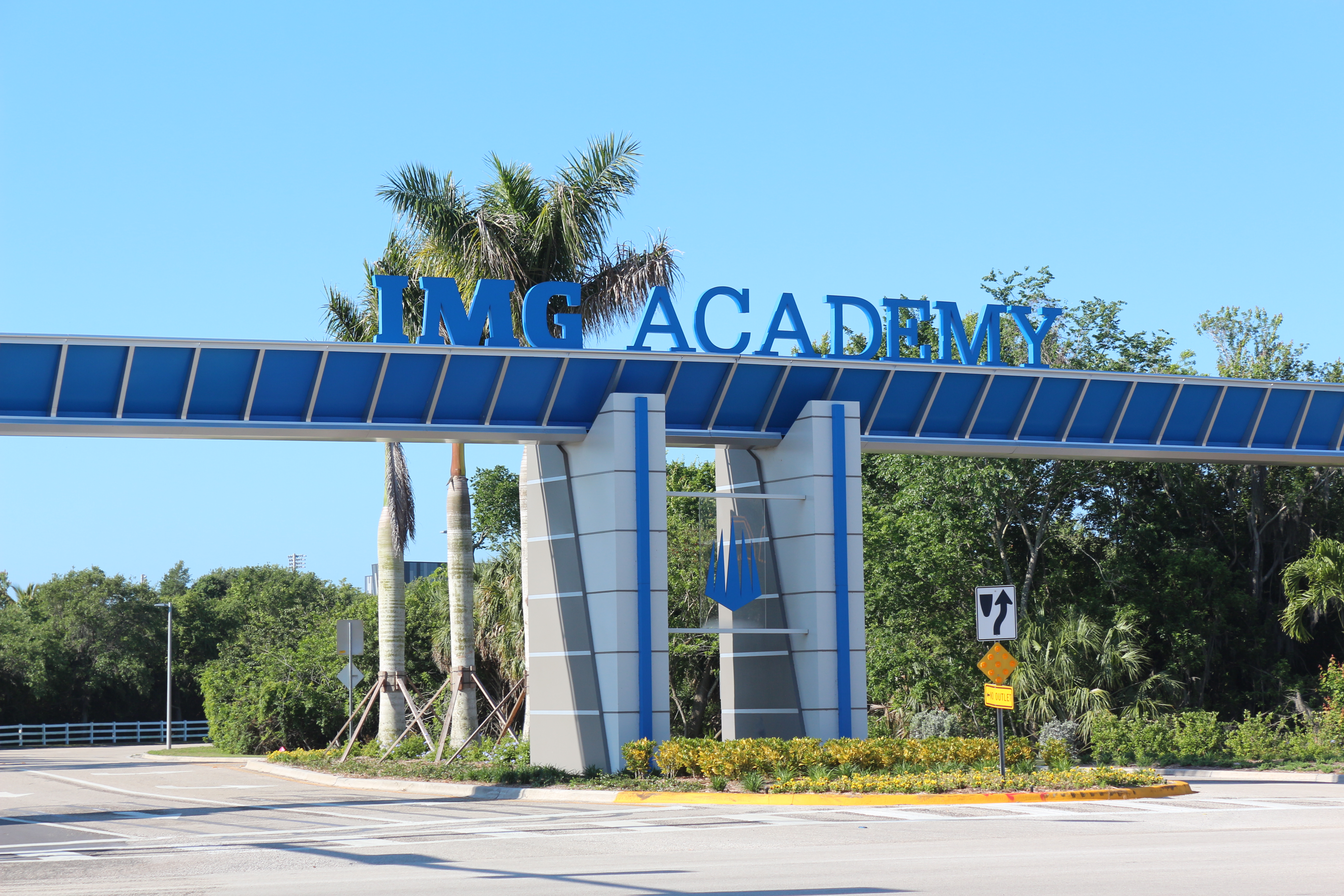 Blue overhead gateway structure reading 'IMG ACADEMY' with palm trees and tropical landscaping.