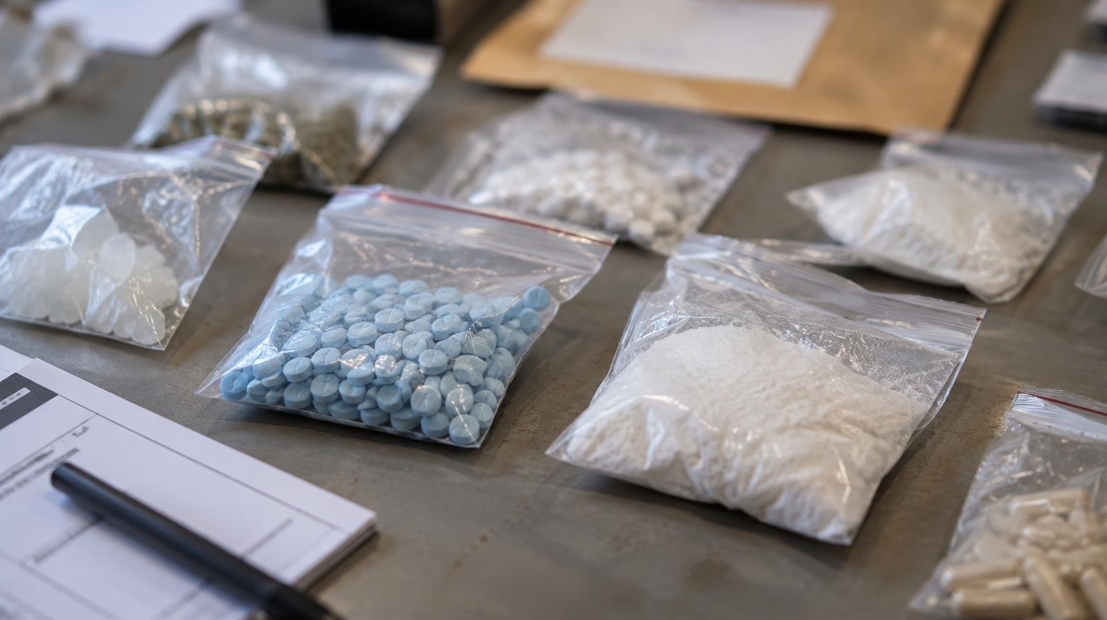 Evidence bags with seized pills and white powder narcotics on a table.